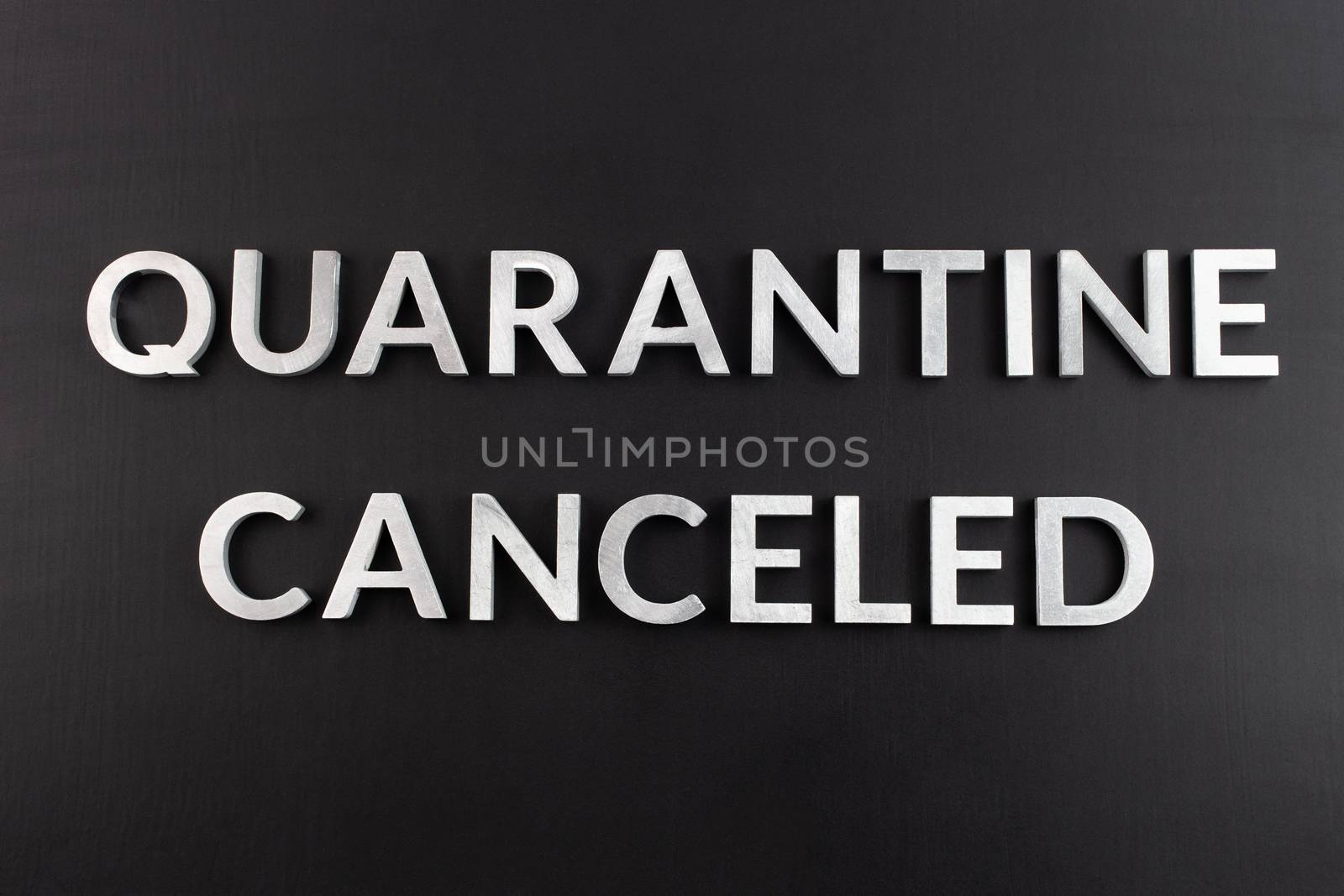 the words quarantine canceled laid with silver metal letters on matte back flat surface directly above in flat lay perspective, end of restrictions concept