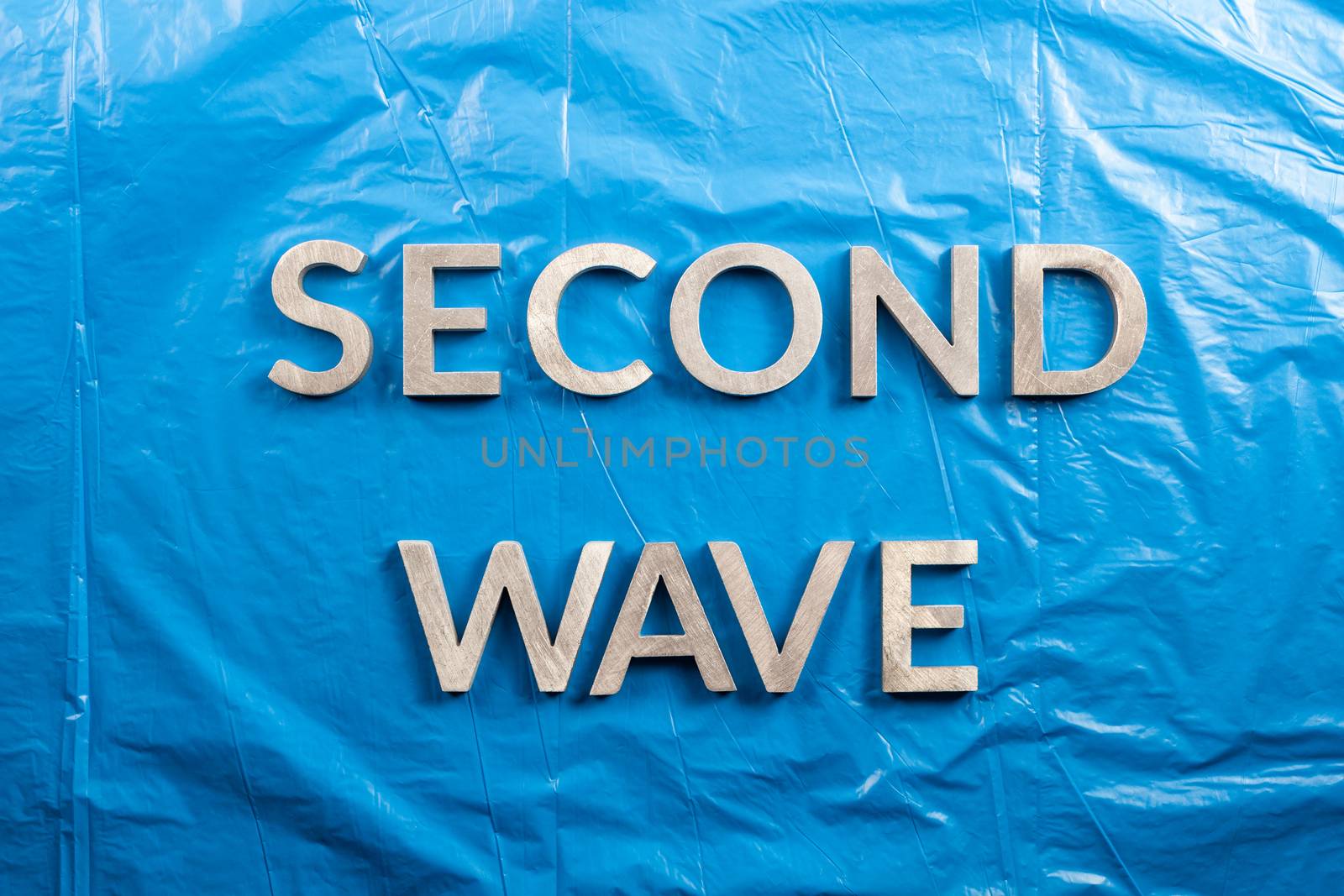the words second wave laid with silver metal letters over crumpled blue plastic film background.