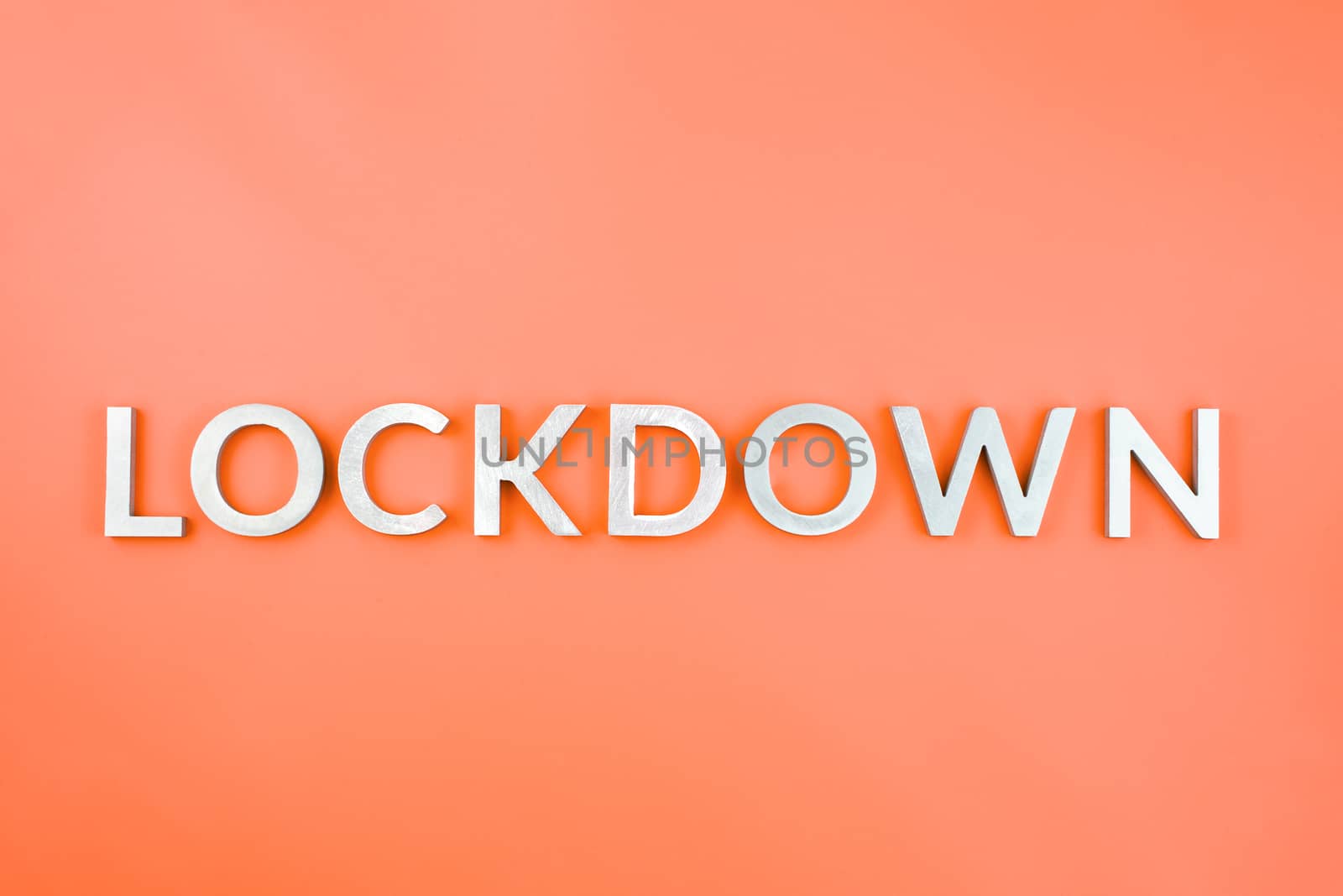 the word lockdown laid with brushed aluminium metal letters on lush lava orange color background in flat lay composition
