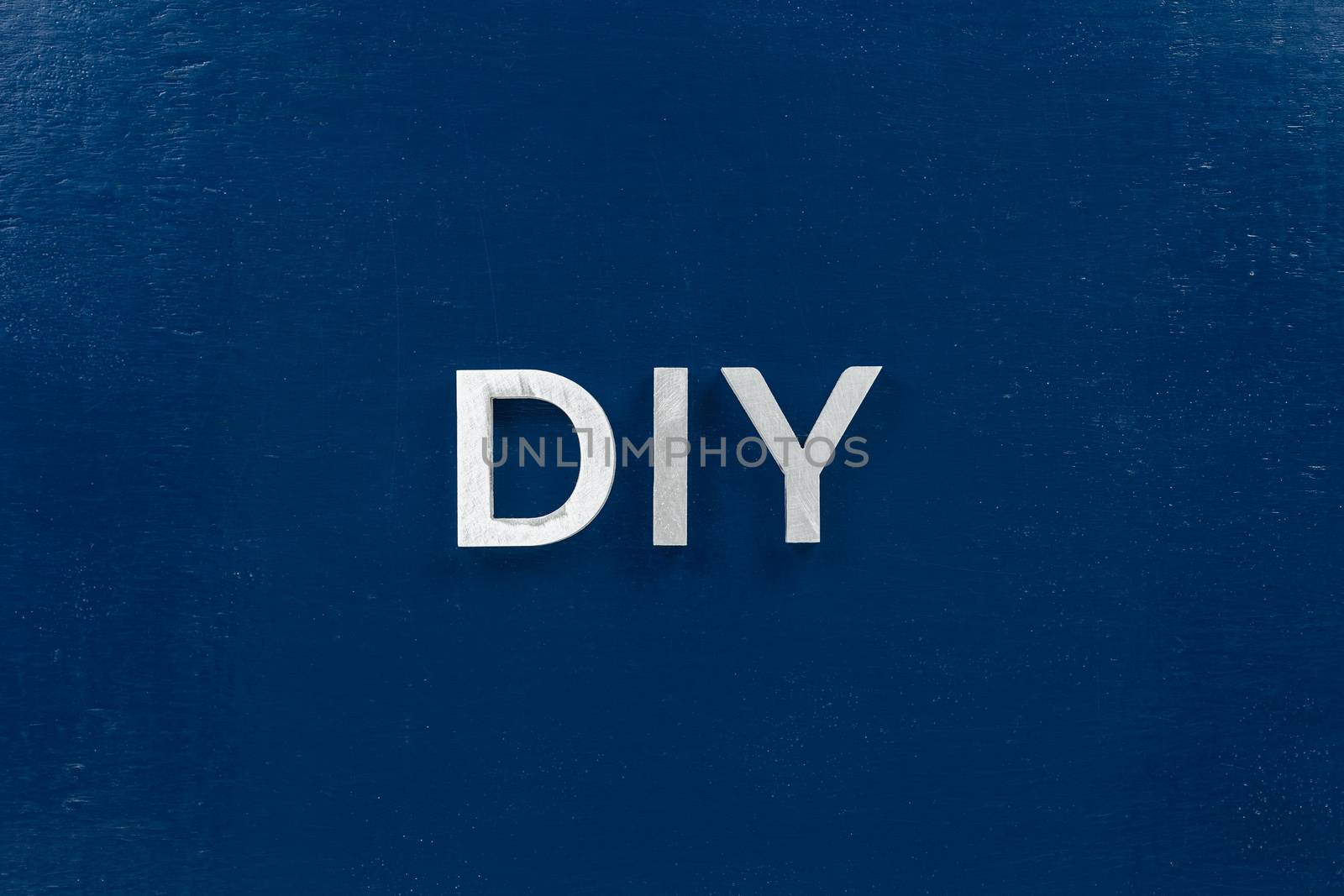 the abbreviation diy - do it yourself - laid with aluminium letters over dark blue flat surface, directly above perspective