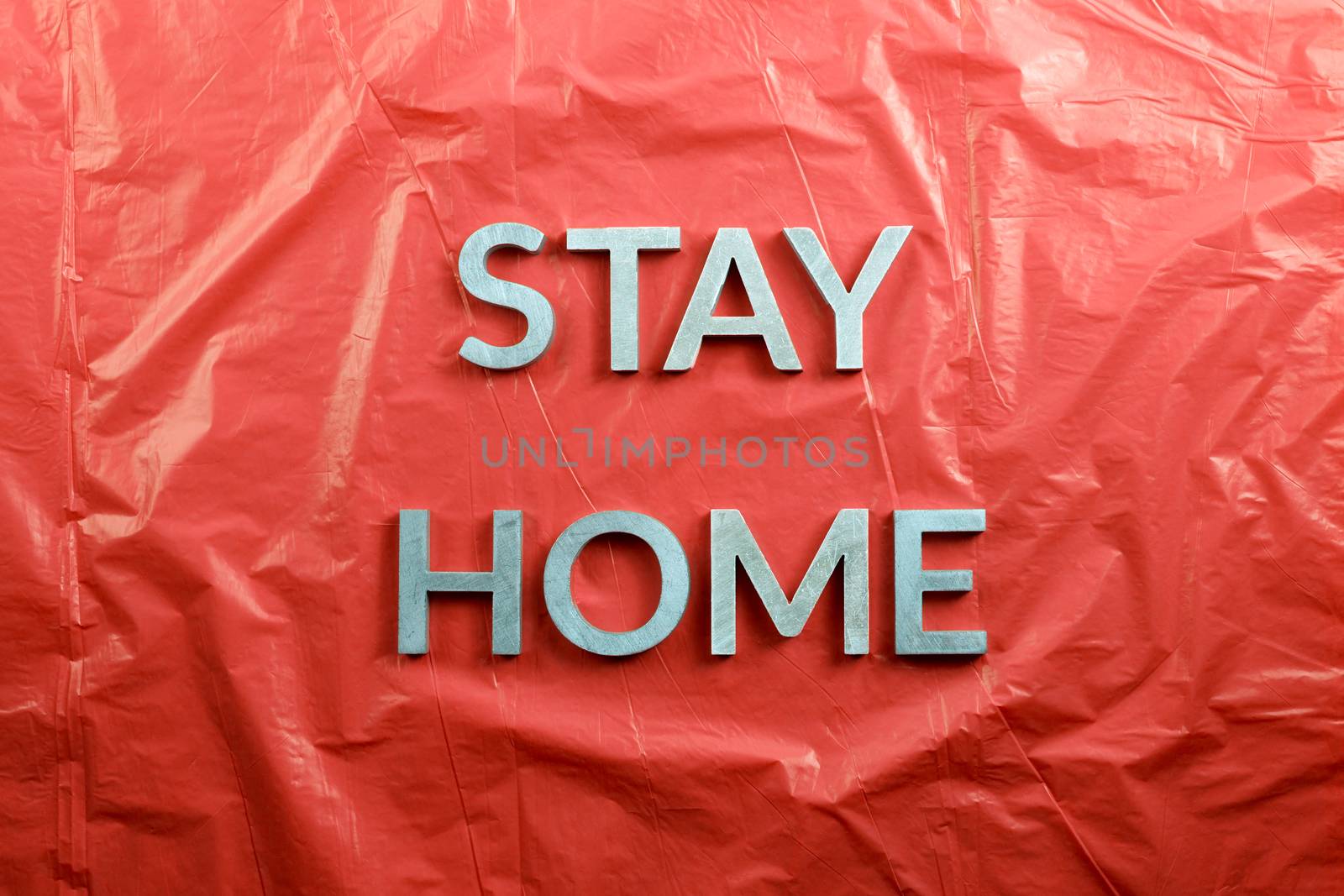 the words stay home laid with silver metal letters on crumpled red plastic background in flat lay perspective by z1b