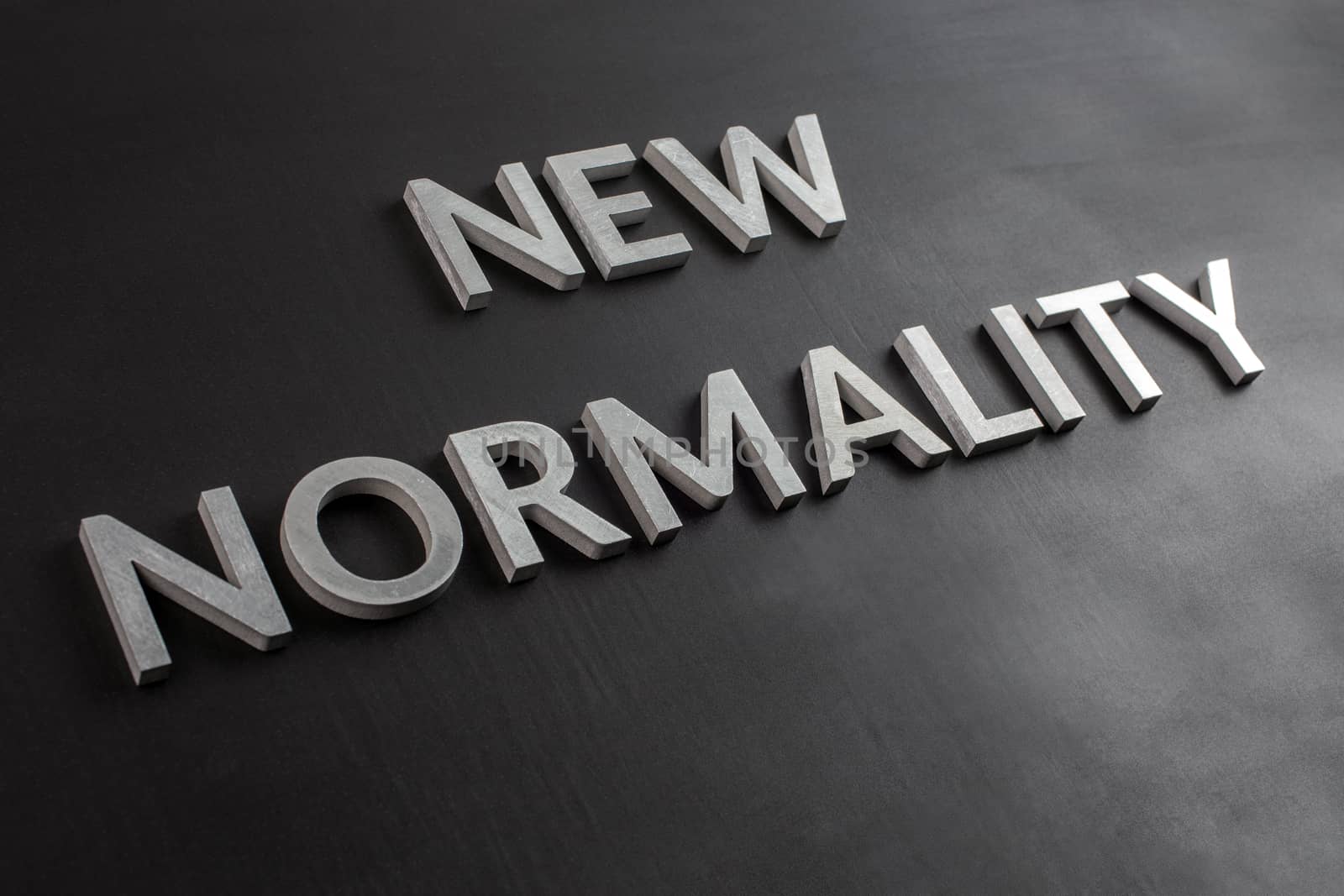 the words new normality laid with silver metal letters on flat black matte surface in slanted diagonal perspective by z1b