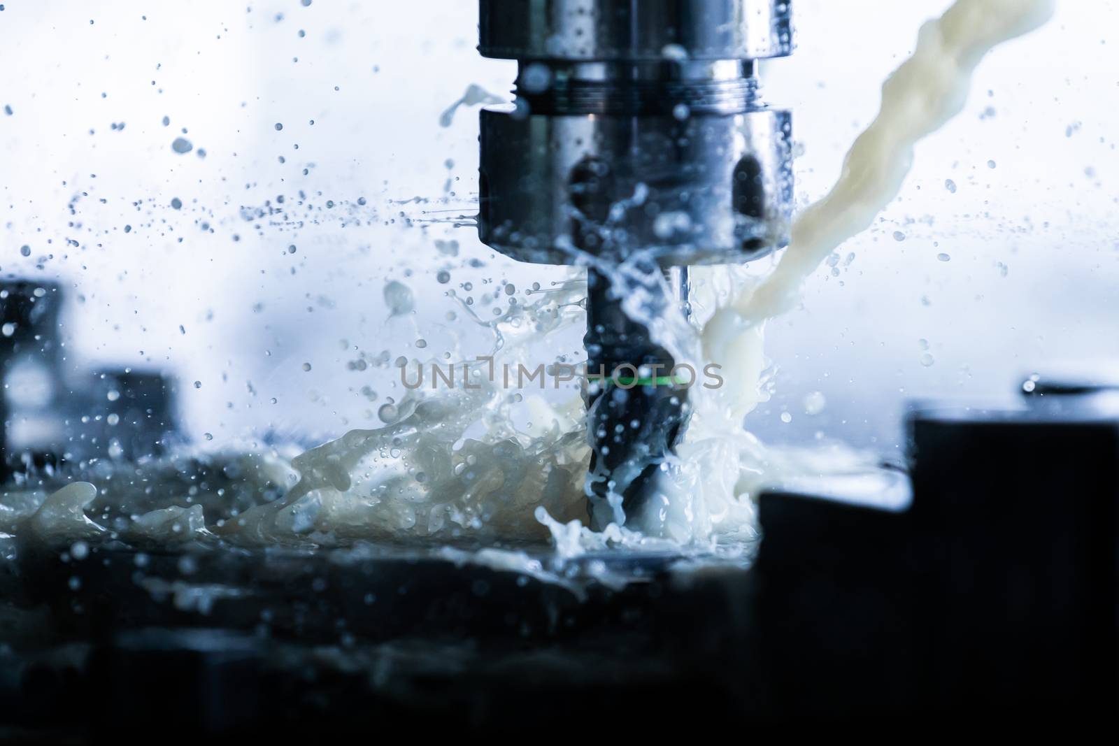 A process of vertical cnc steel milling with external water coolant streams, splashes and a lot of metal chips. Fast shutter speed for motion freezing.