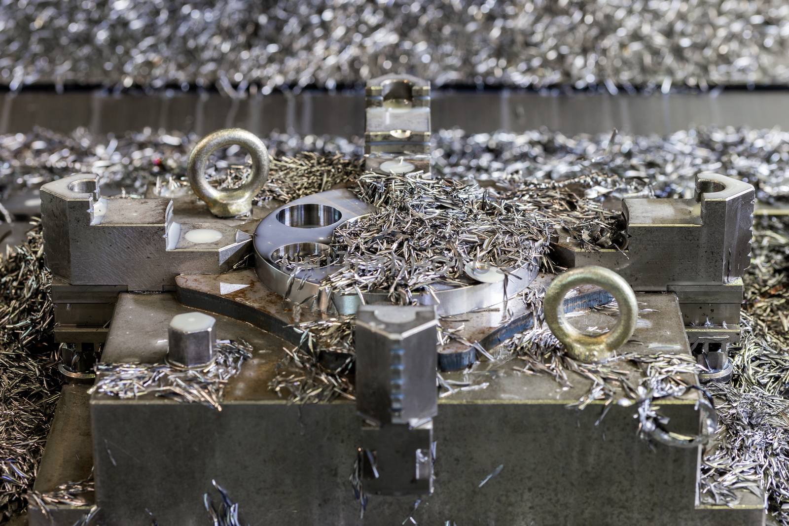 a lot of swarf and iron chips after cnc milling on workpiece and 4-jaw chuck holder - close-up with selective focus and background blur