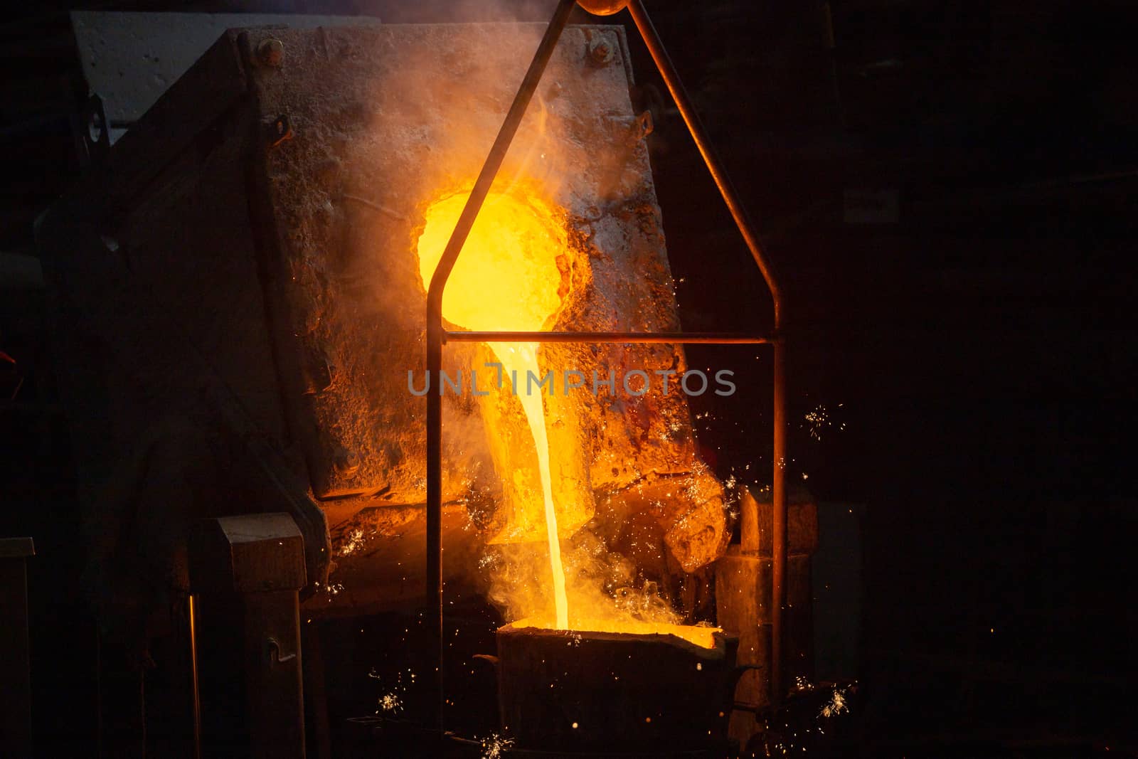 a process of ladle filling with molten hot steel from furnace with smoke - close-up with selective focus and background blur