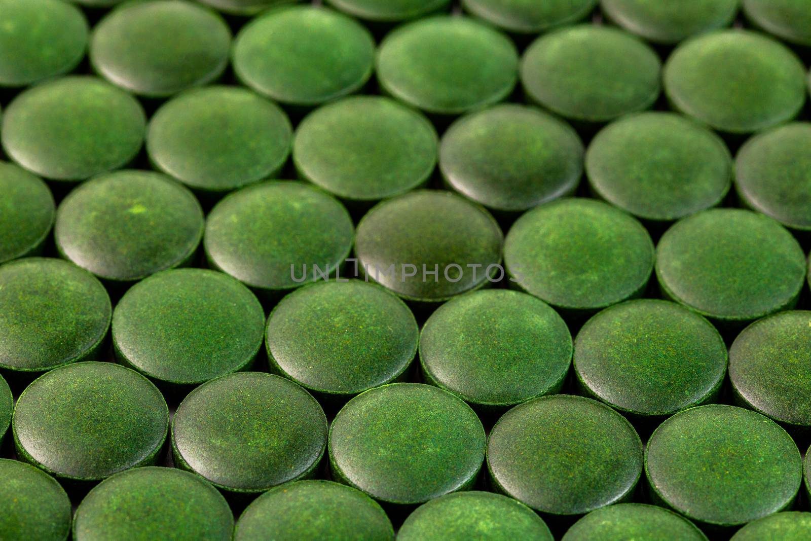 close-up background of many green organic spirulina tablets laid tight in one layer on flat surface.