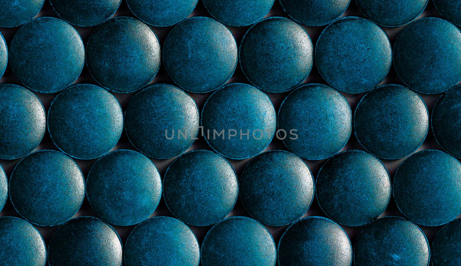 a seamless hexagonal pattern of many blue organic spirulina tablets laid tight in one layer on flat surface.