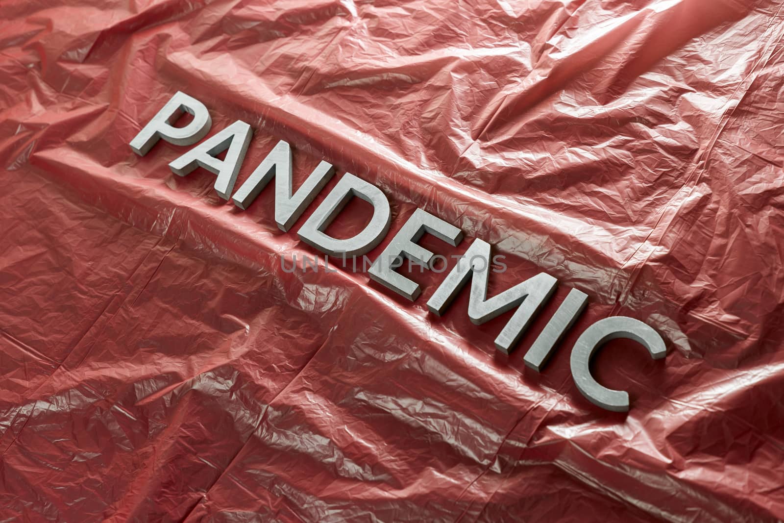 the word pandemic laid with silver letters on crumpled red plastic film - diagonal perspective composition with selective focus and dramatic light