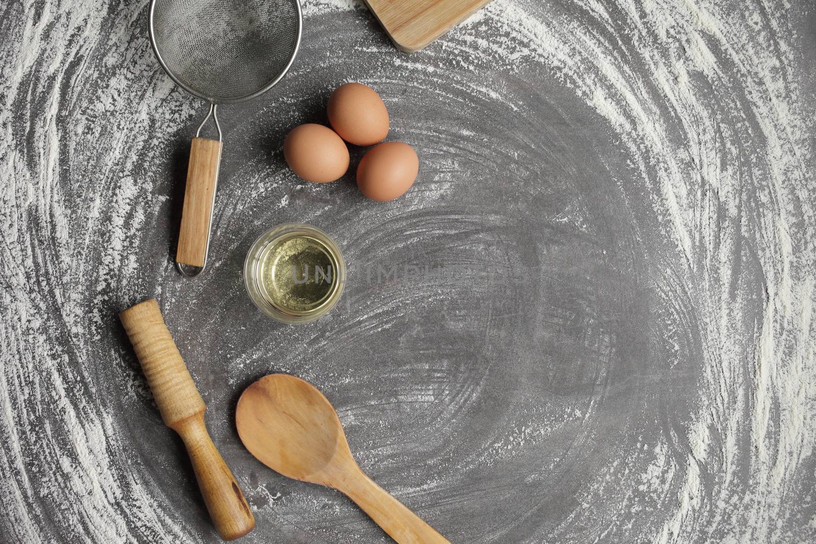 Chicken egg, flour, olive oil, kitchen tool on gray table background. Products for baking bakery products. Cutting board, rolling pin, flour sieve, wooden spoon. For bread or cake