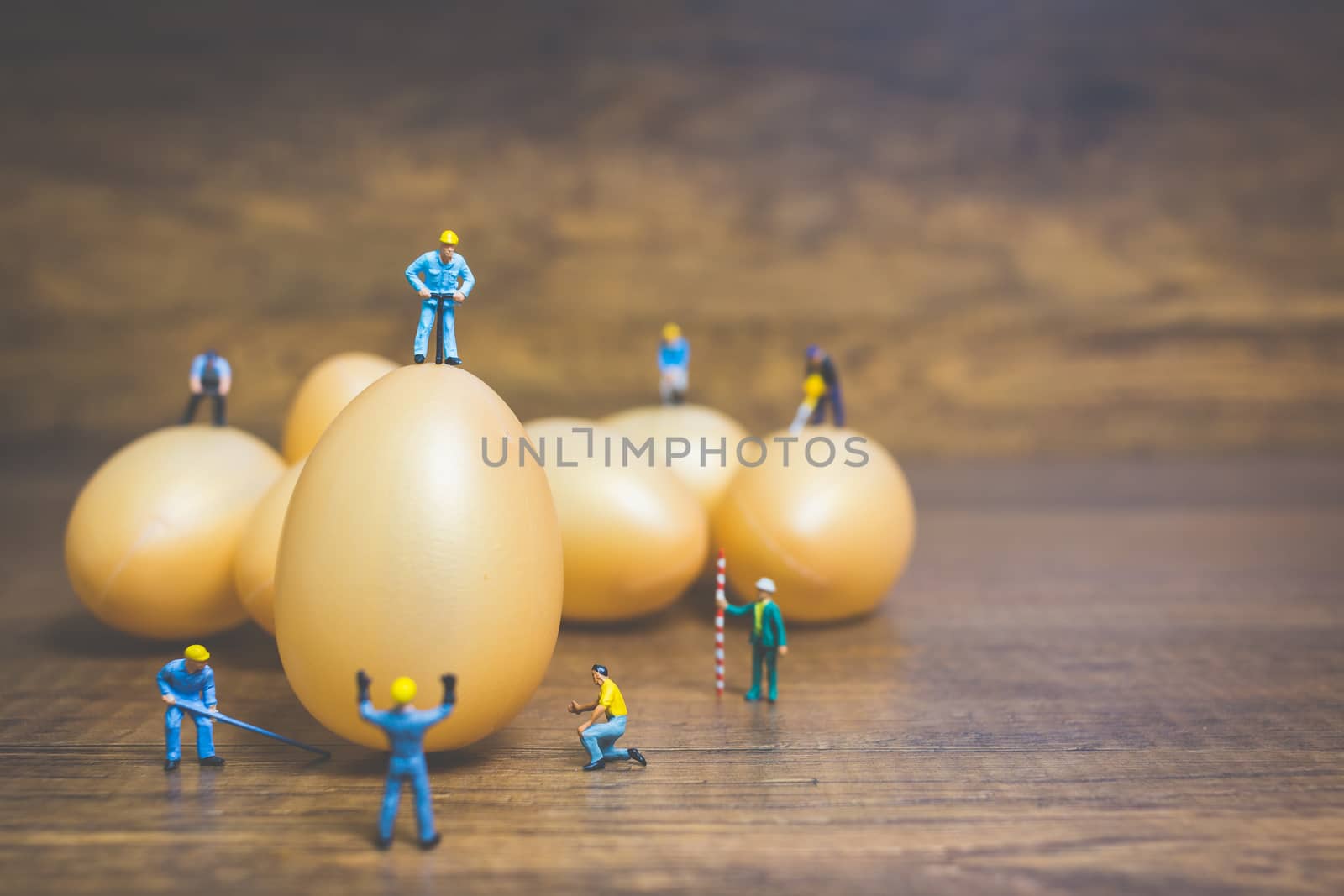 Miniature people work at Easter-eggs for Easter day on wooden background