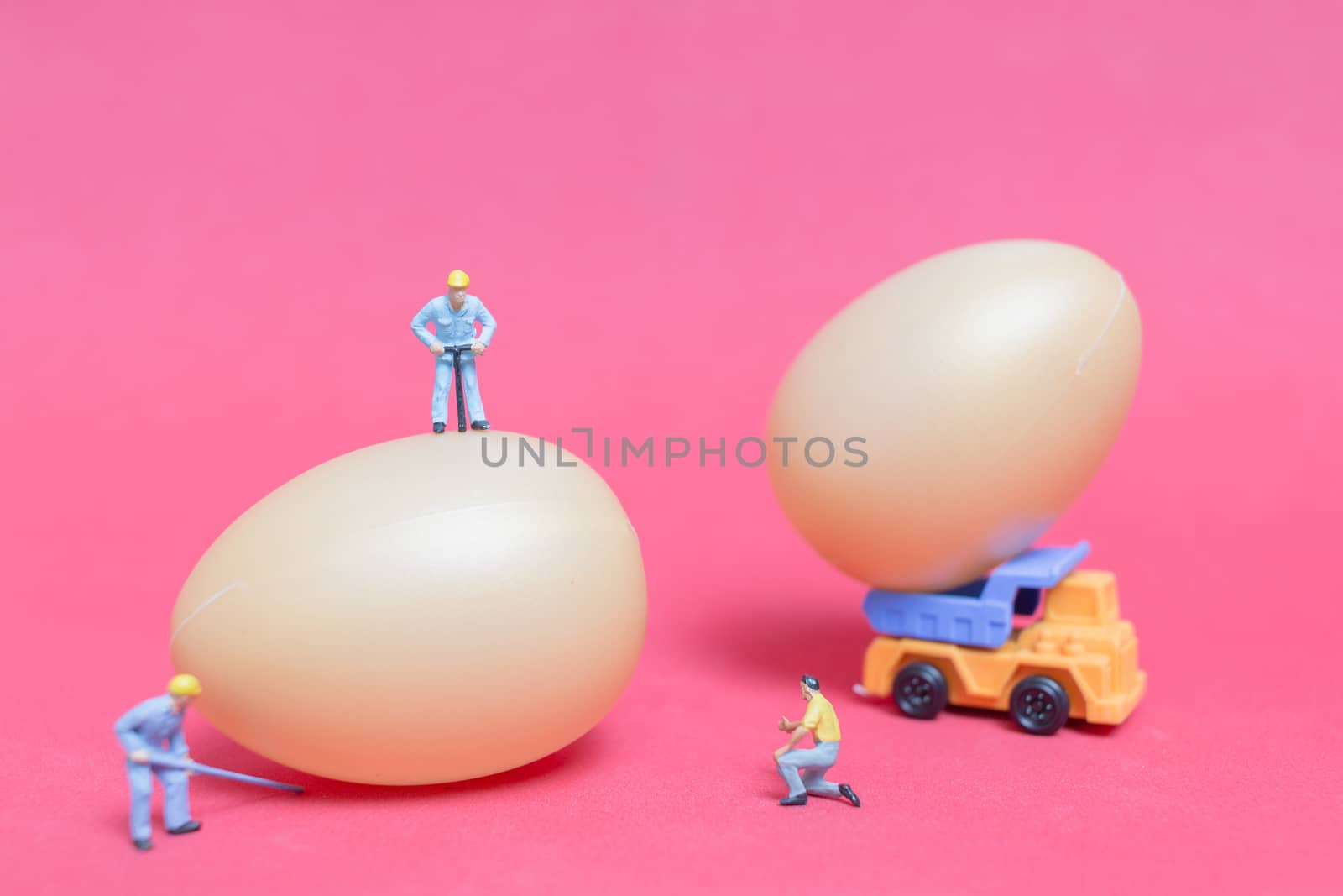 Miniature people work at Easter-eggs for Easter day on pink background