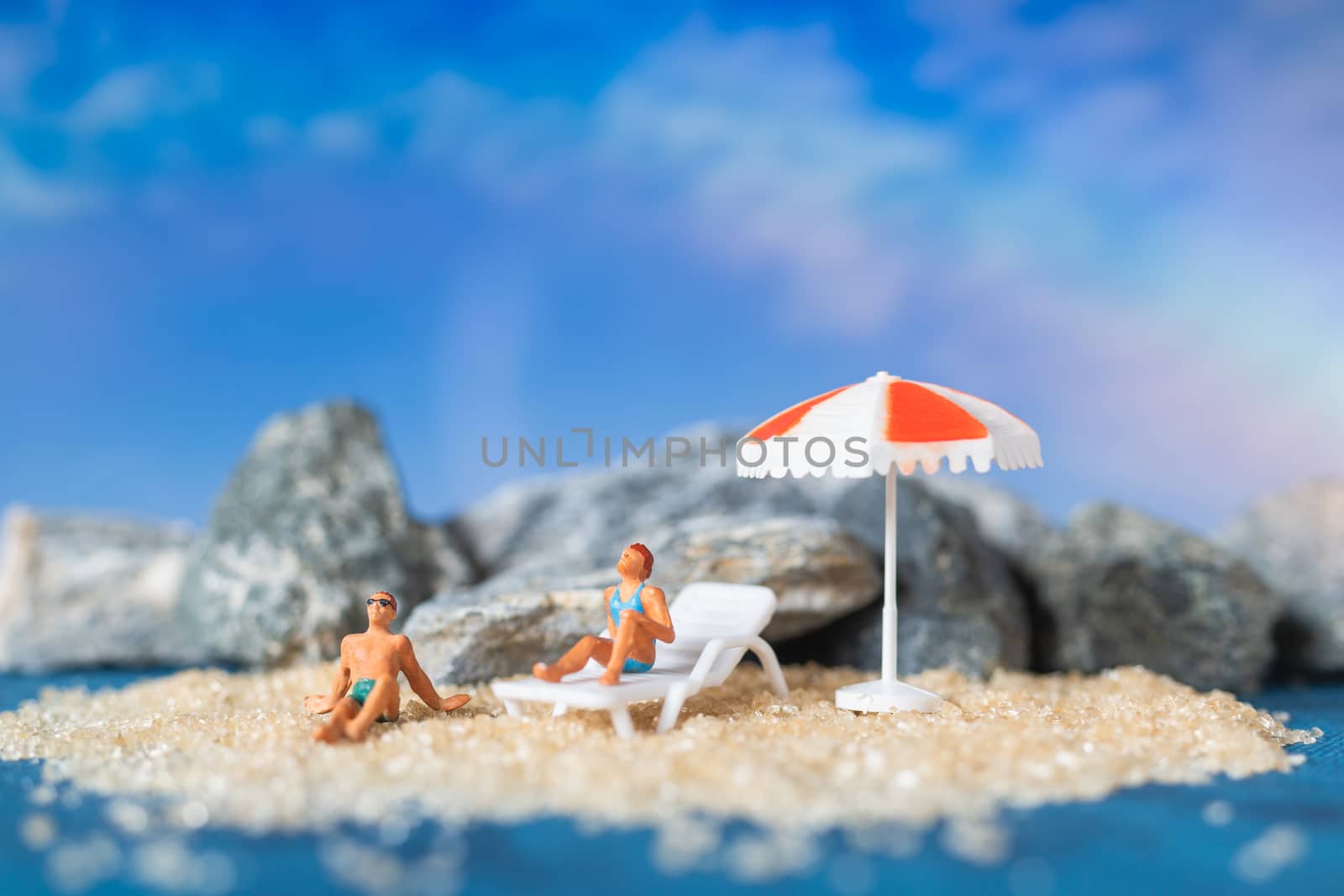 Miniature people wearing swimsuit relaxing on the beach with blue background , Summer time concept