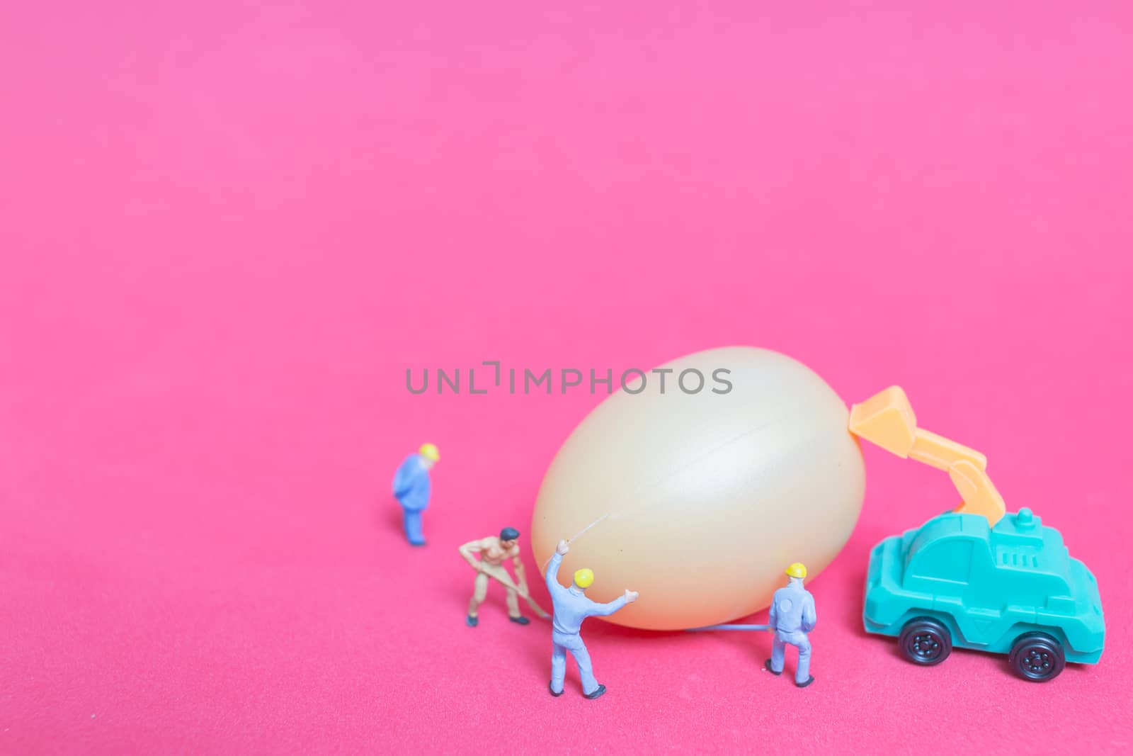 Miniature people work at Easter-eggs for Easter day on pink background