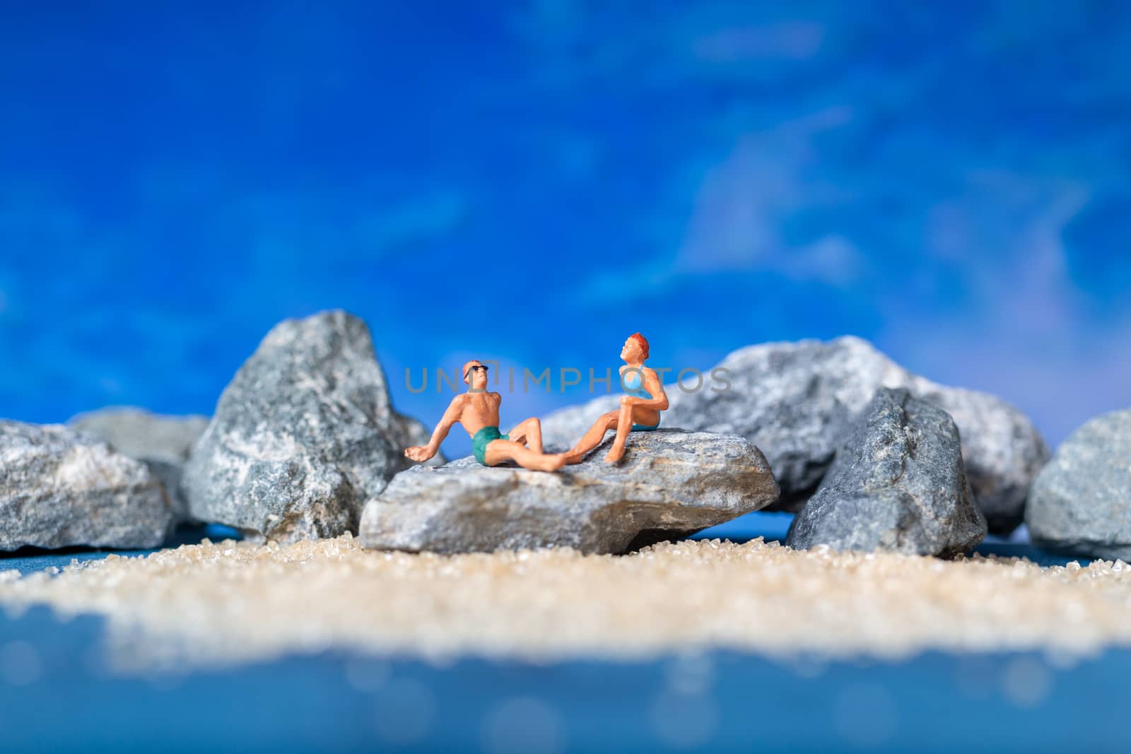 Miniature people wearing swimsuit relaxing on the beach with blue background , Summer time concept