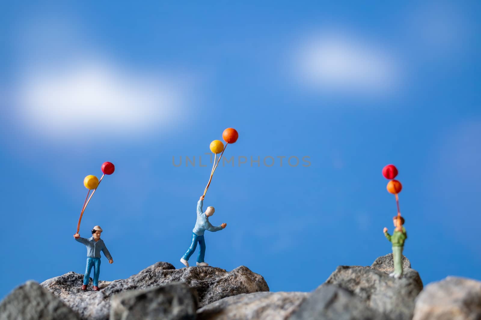 Miniature people , Happy family holding balloon on The rock with blue sky background