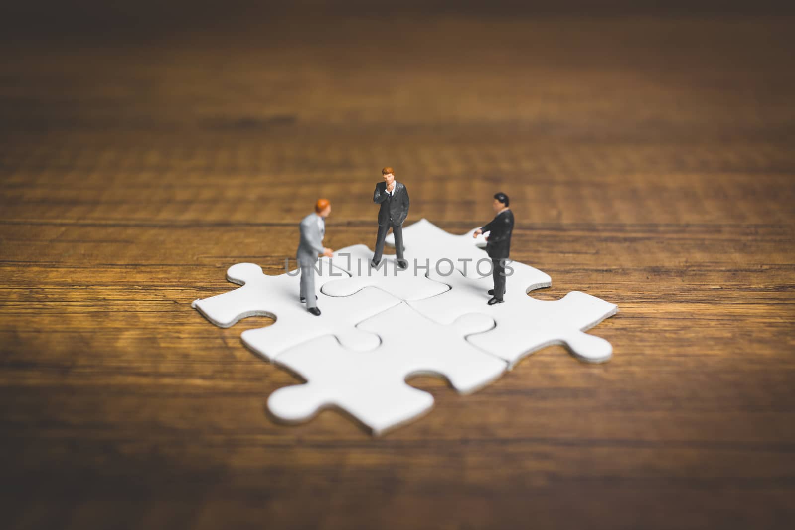 Miniature people: Businessman standing on jigsaw with wooden background : Business concept.