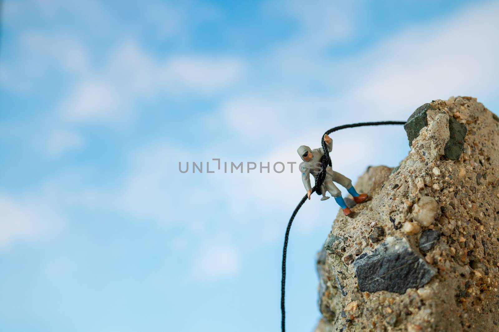Miniature people: Hikers climbing up on the rock . Sport and leisure concept.