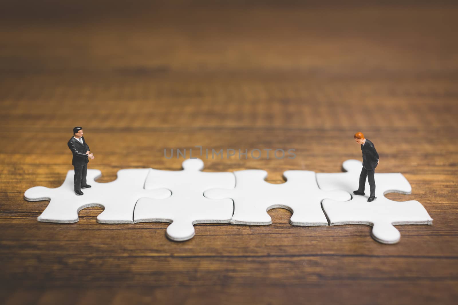 Miniature people: Businessman standing on jigsaw with wooden background : Business concept.