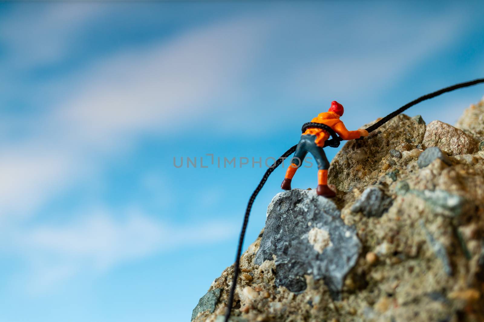 Miniature people: Hikers climbing up on the rock . Sport and leisure concept.