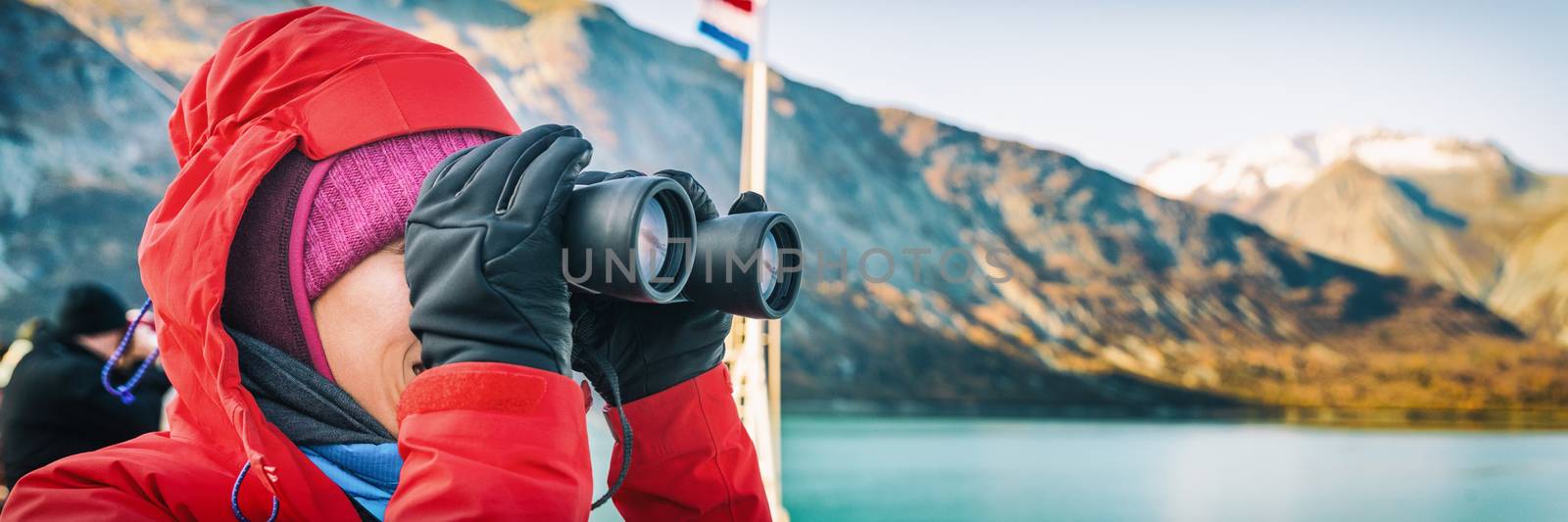 Alaska cruise travel tourist whale watching on boat shore excursion ride at Glacier Bay landscape. Woman looking at view binoculars on cruise ship. Panoramic banner portrait.