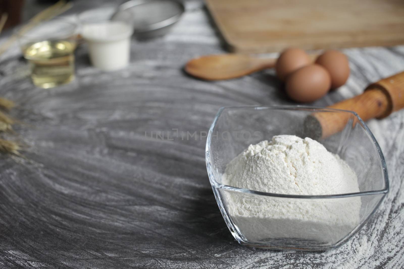 Flour, egg, olive oil, milk, wheat ears, kitchen tool on gray table background. by selinsmo