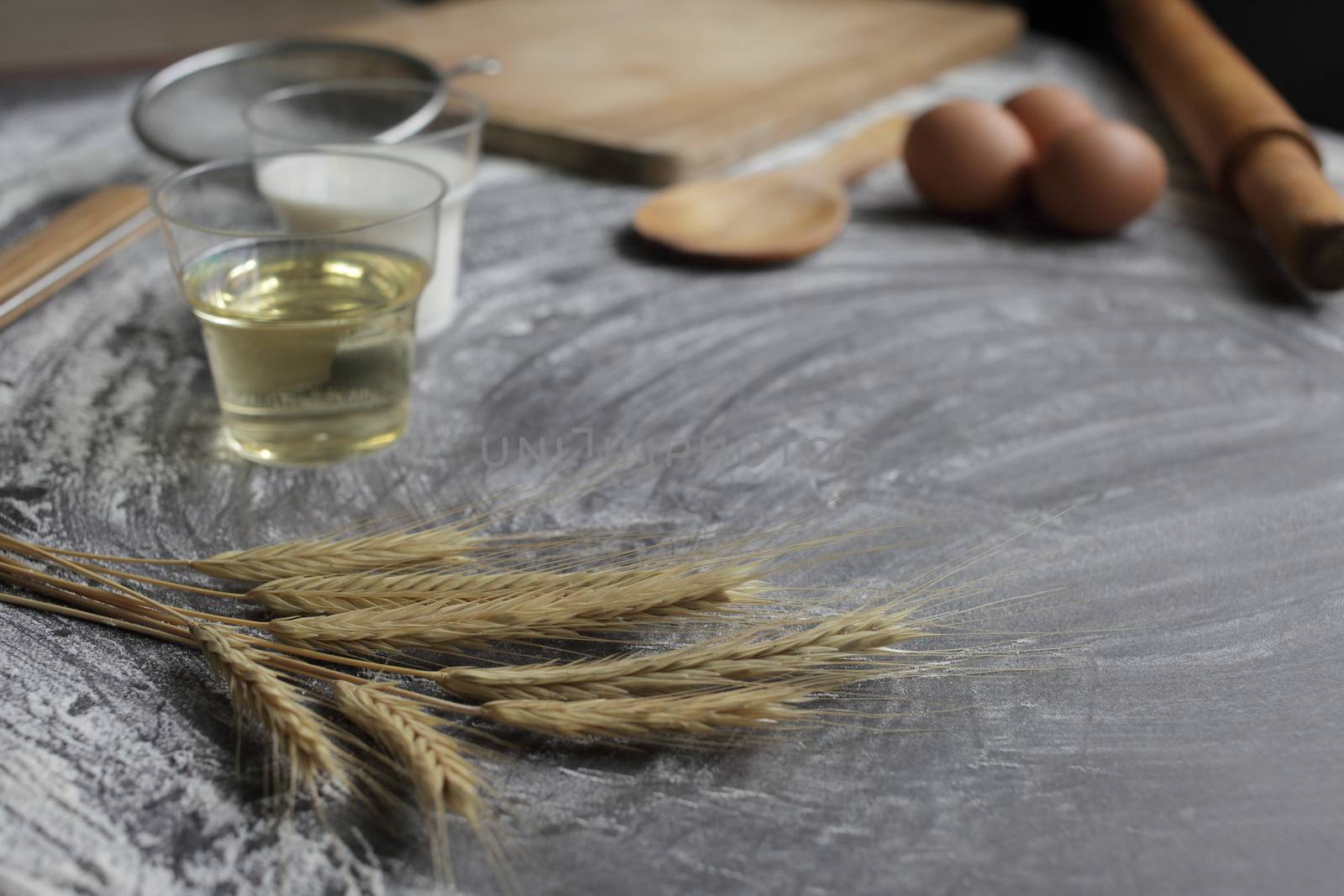 Chicken egg, flour, olive oil, milk, wheat ears, kitchen tool on gray table background. Products for baking bakery products. Cutting board, rolling pin, flour sieve, wooden spoon. For bread or cake