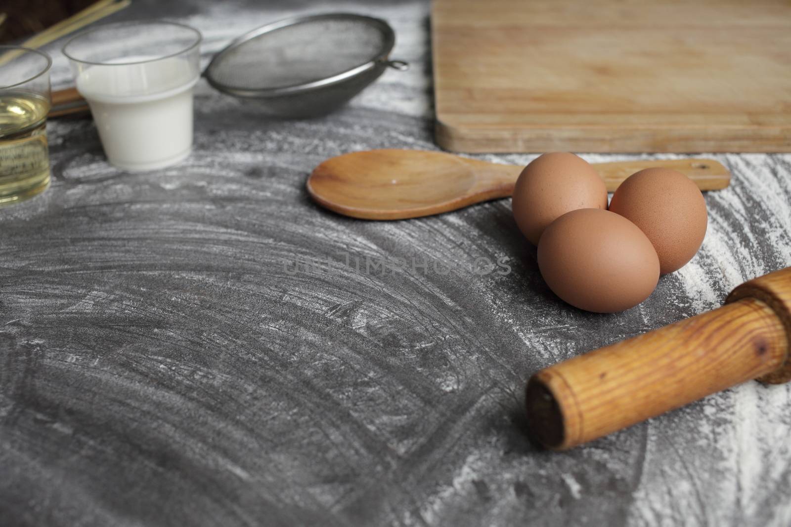 Chicken egg, flour, olive oil, milk, wheat ears, kitchen tool on gray table background. Products for baking bakery products. Cutting board, rolling pin, flour sieve, wooden spoon. For bread or cake