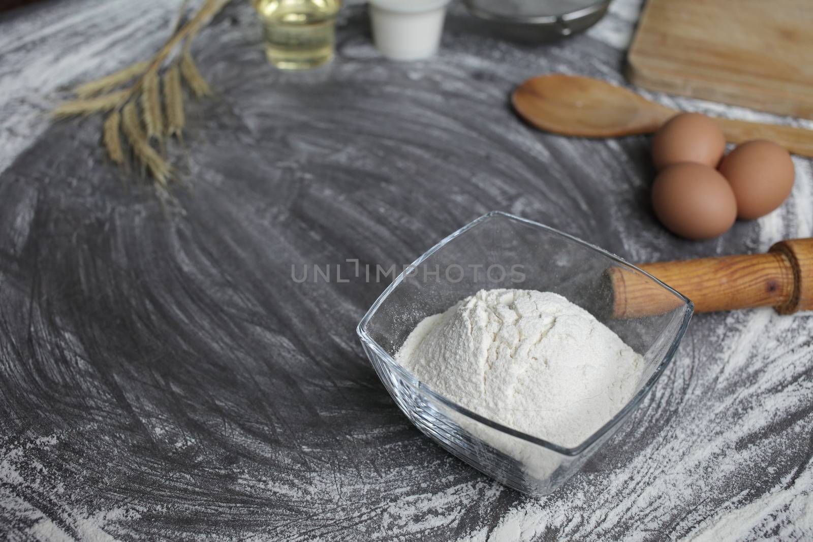 Flour, egg, olive oil, milk, wheat ears, kitchen tool on gray table background. by selinsmo