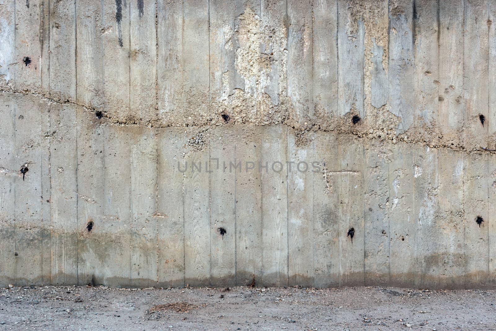 an outdoor thick rough gray concrete wall with part of floor surface, visible imprints of wooden planks, twice filled