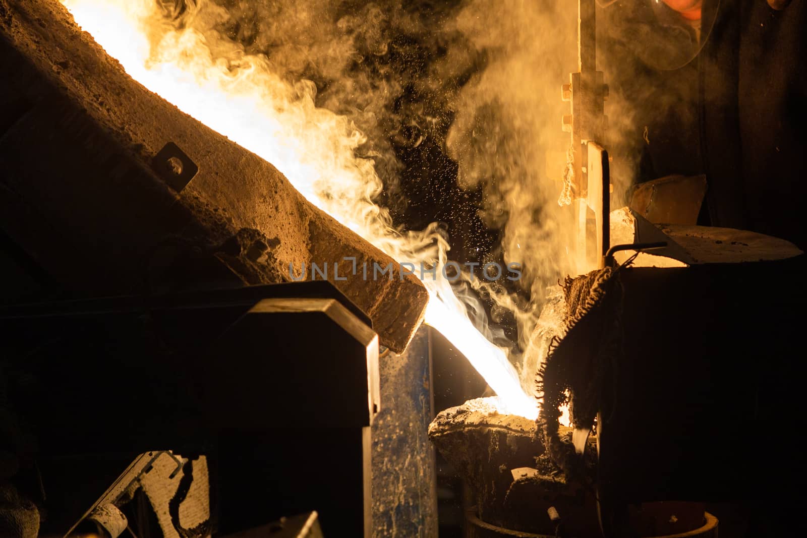 a process of ladle filling with molten hot steel from furnace with smoke - close-up with selective focus and background blur