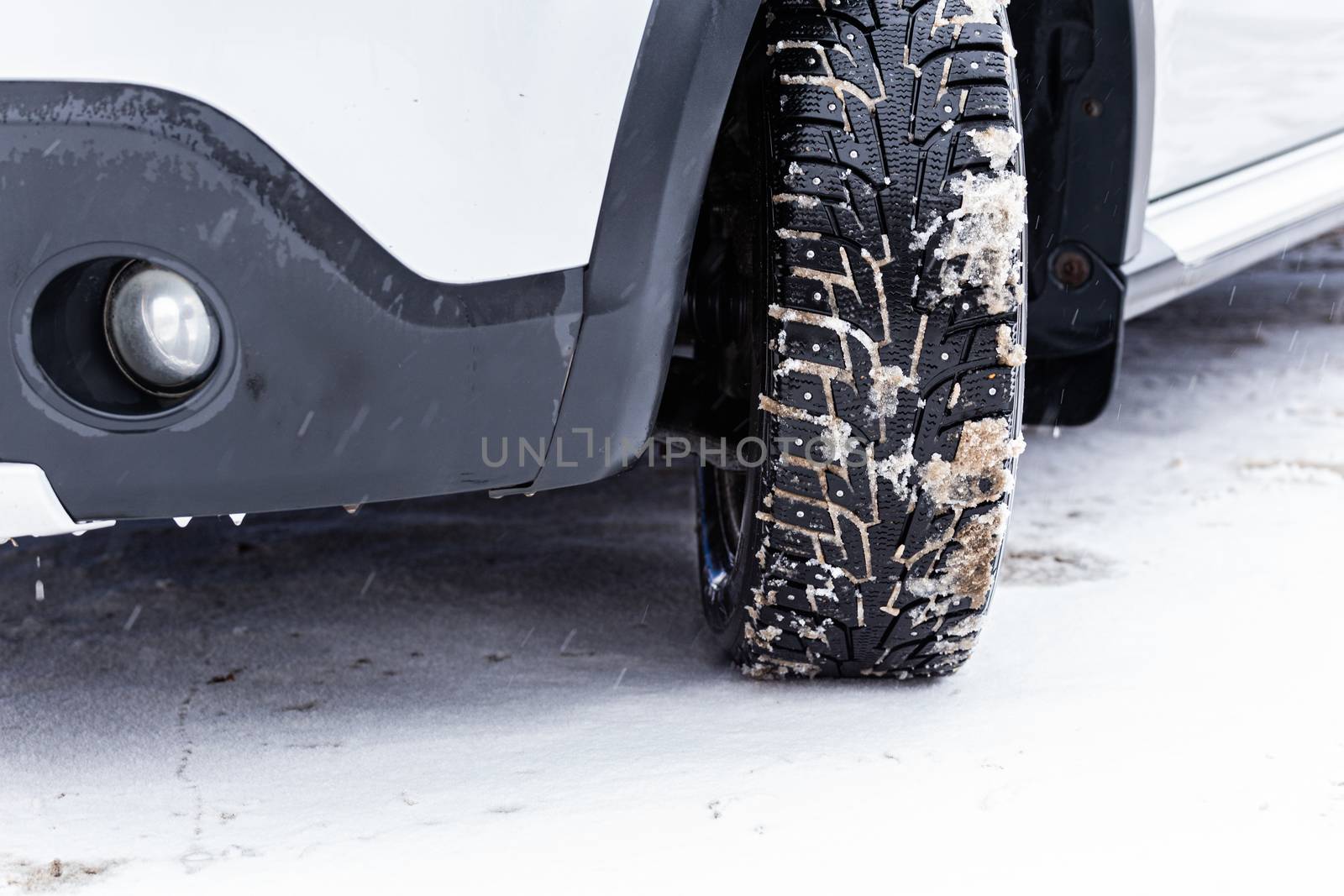 an unadorned picture of winter car wheel with metal spikes on snow close-up.