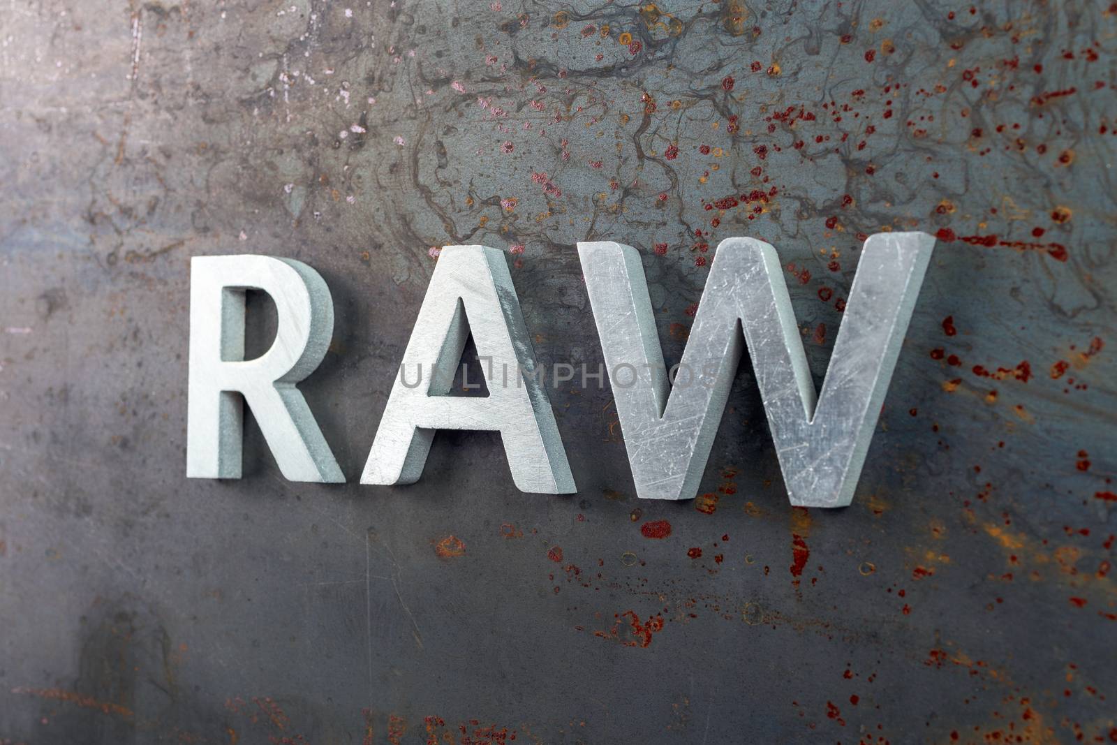 the word raw laid with silver metal letters on hot rolled steel sheet surface - close-up with selective focus and skewed perspective