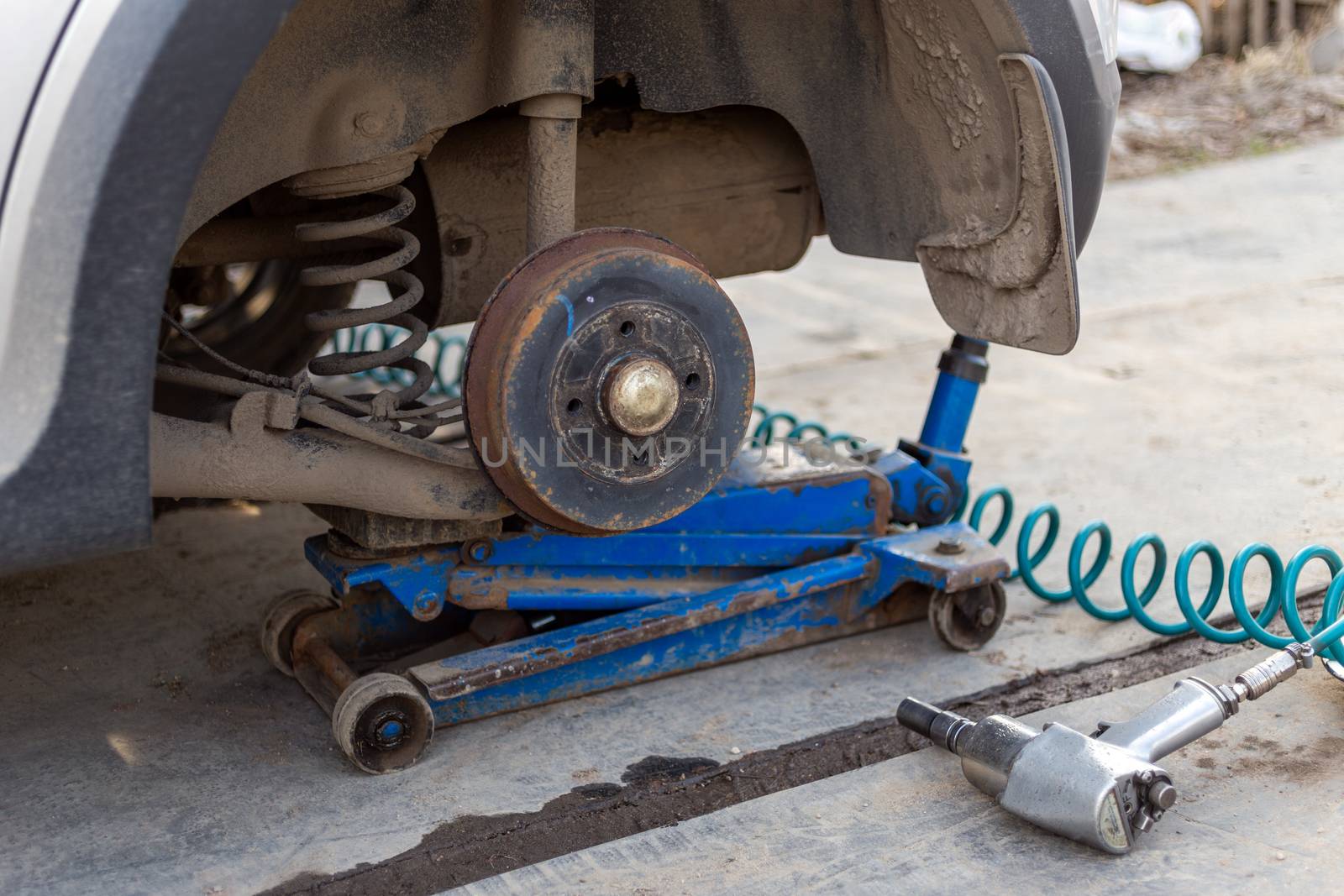 Car without wheel lifted with hydraulic floor jack and pneumatic impact wrench in a outdoor car workshop. Season tire changing procedure. by z1b