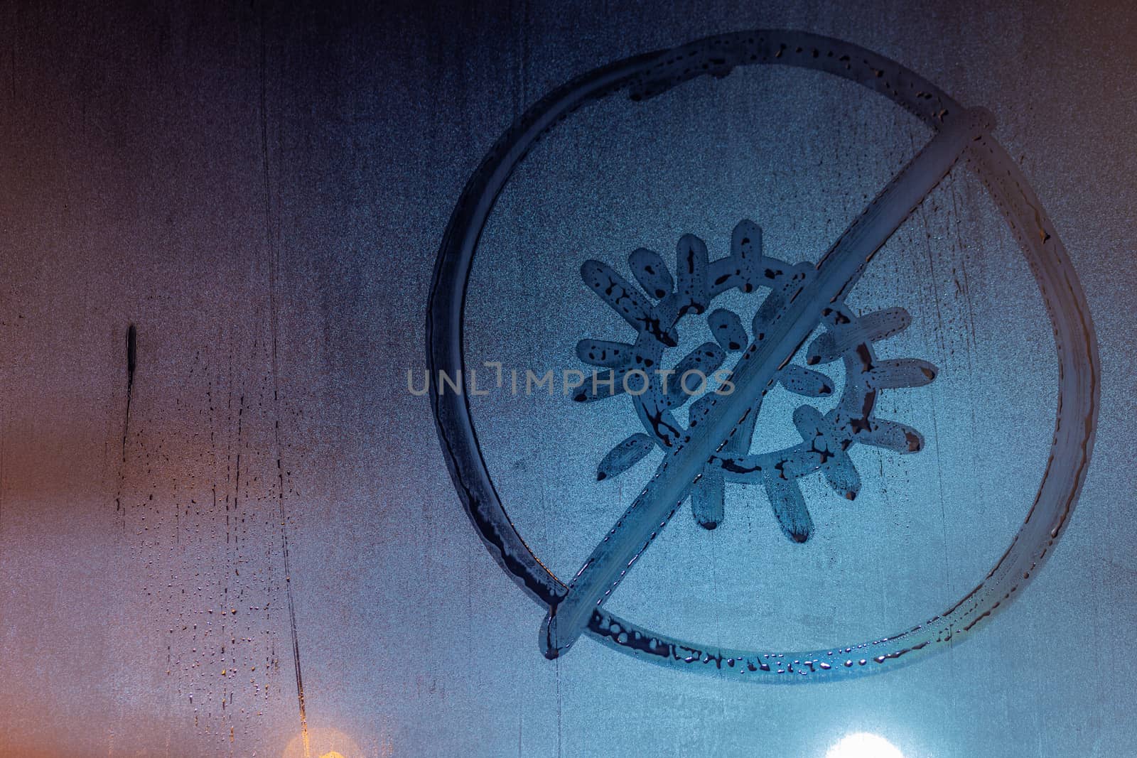 banned coronavirus icon handwritten on night wet window glass close-up with selective focus and background blur