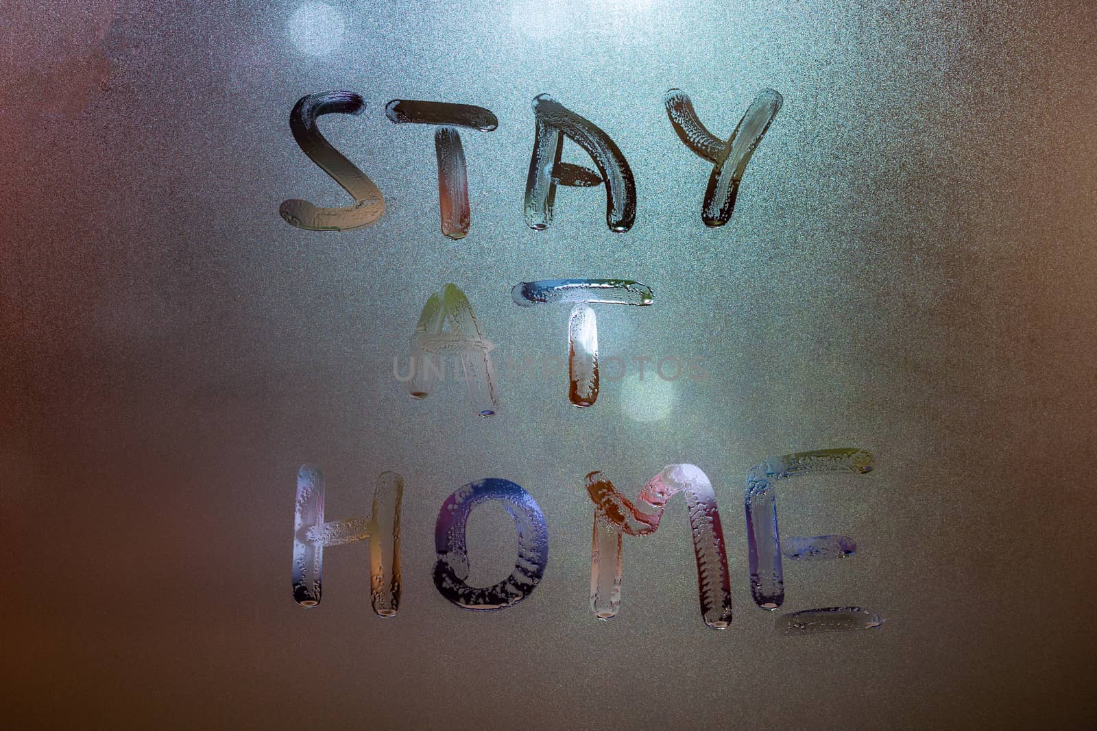 the words stay at home handwritten on wet window glass at night - close-up full frame picture with selective focus and background blur