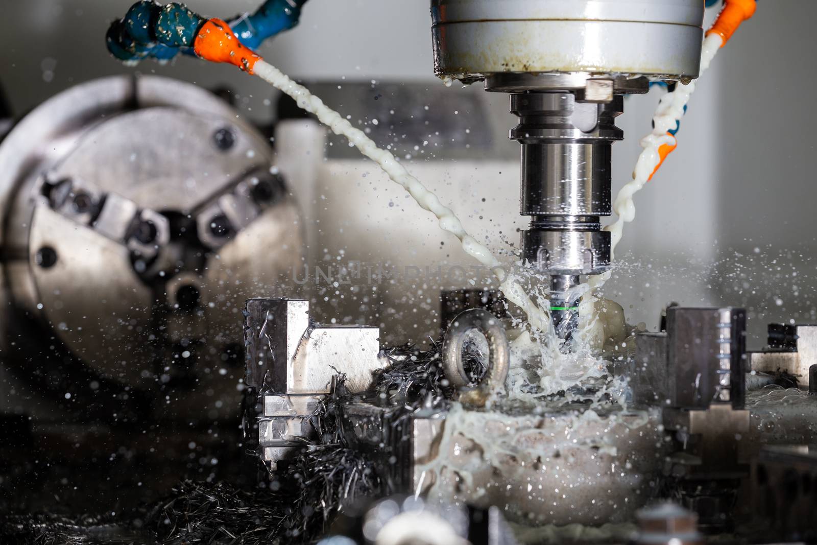 A process of vertical cnc steel milling with external water coolant streams, splashes and a lot of metal chips. Fast shutter speed for motion freezing.