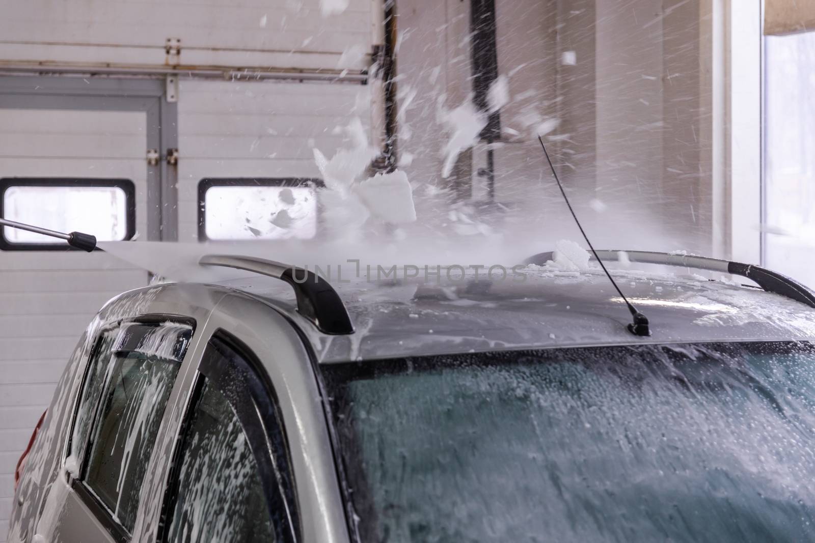 Indoor self car washing. Process of removing soap foam from roof of vehicle with high pressure water stream - close-up vith selective focus and motion blur.