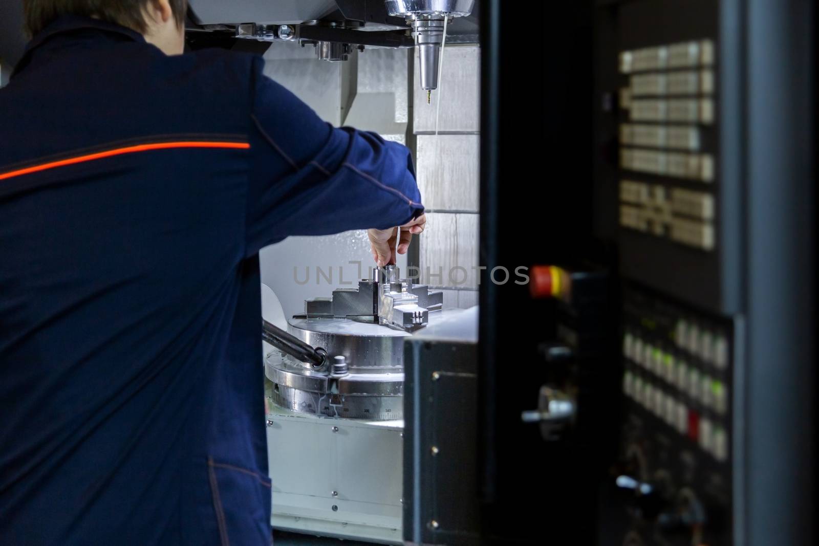 The operator of 5-axis cnc milling machine changes the workpiece in collet chuck. Selective focus on background, blur on foreground,