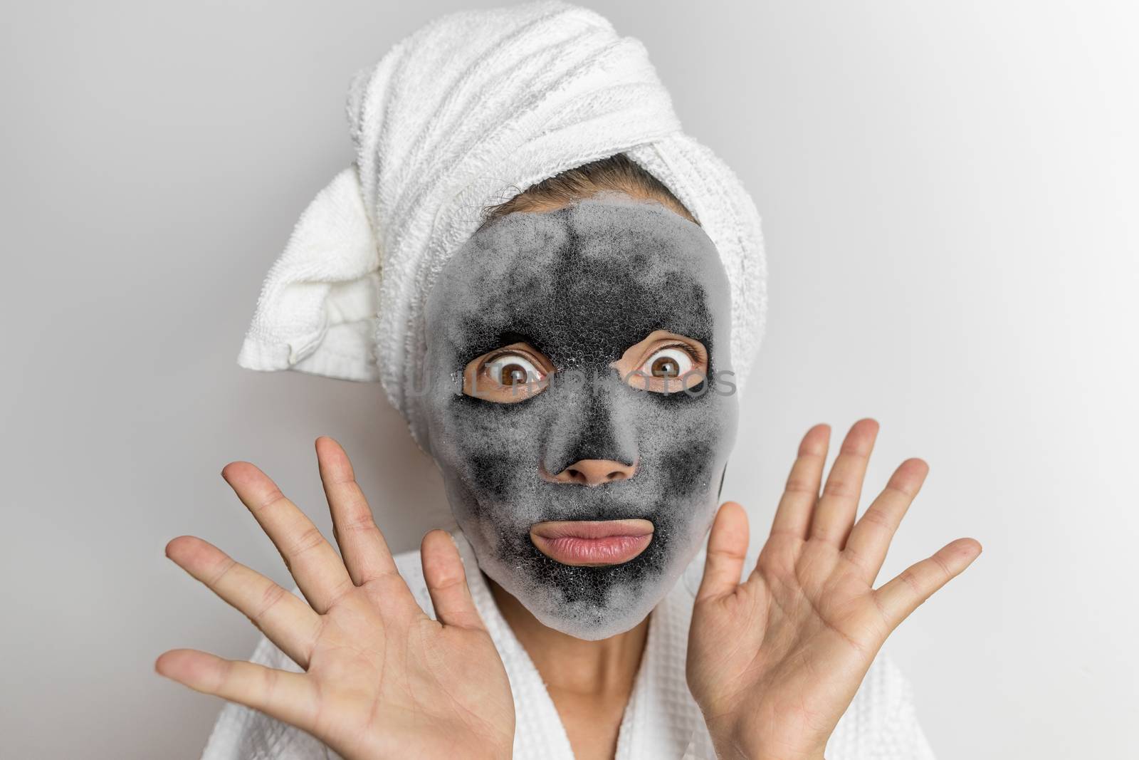 Face mask bubble foam facial funny woman at beauty spa looking shocked or surprised, scary chemicals in beauty products. Asian girl wearing bath towel on hair.