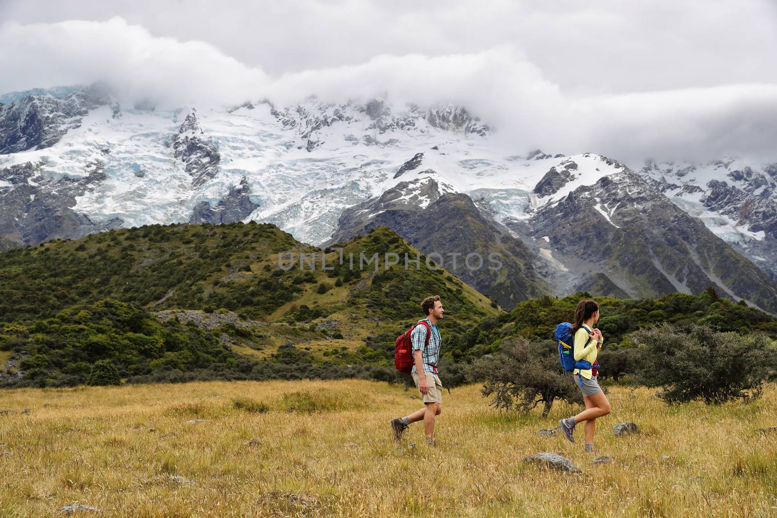 New Zealand travel hikers hiking on snow capped mountains landscape background. Couple trampers walking on Hooker Valley Track, popular tourist destination for summer vacation by Maridav