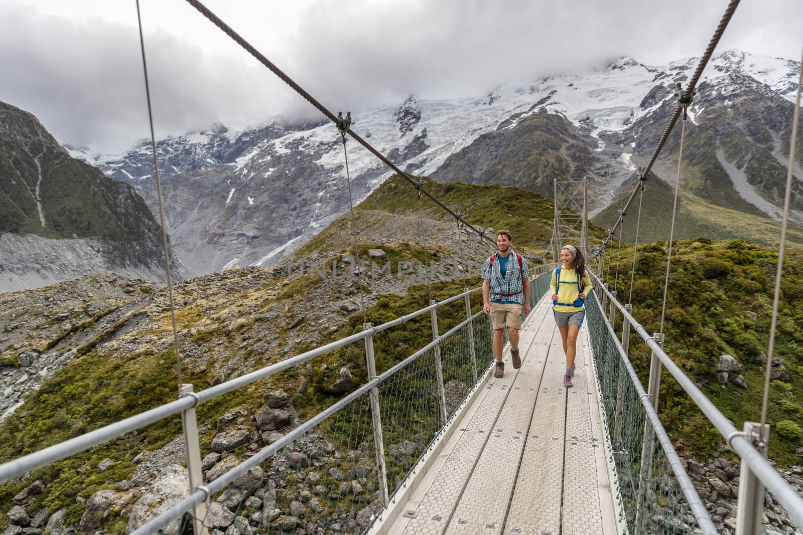 Hooker Valley Track hiking trail, New Zealand. Hikers people crossing bridge on the Hooker Valley track, Aoraki, Mt Cook National Park with snow capped mountains landscape.