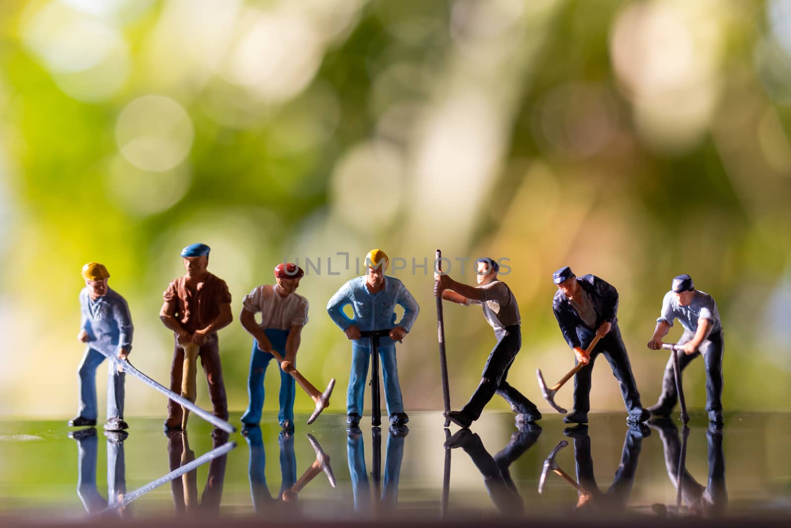Miniature people worker holding tool outdoors with green bokeh background , Construction concept