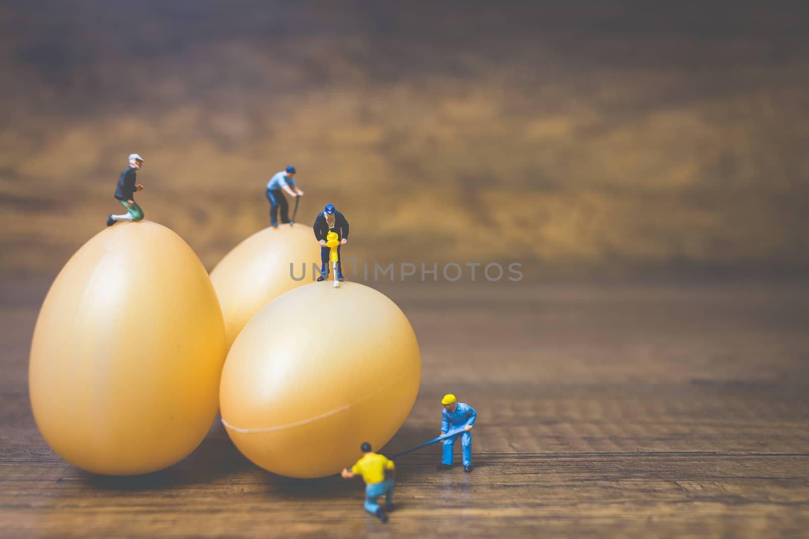 Miniature people work at Easter-eggs for Easter day on wooden background