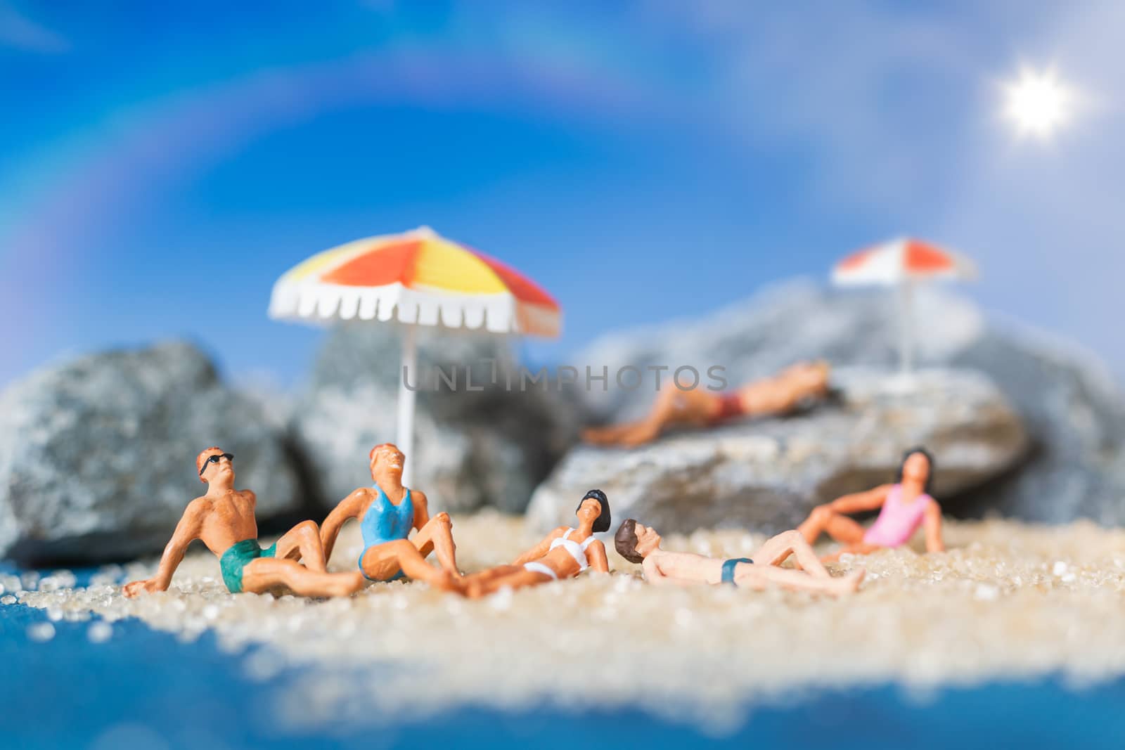 Miniature people wearing swimsuit relaxing on the beach with blue background , Summer time concept