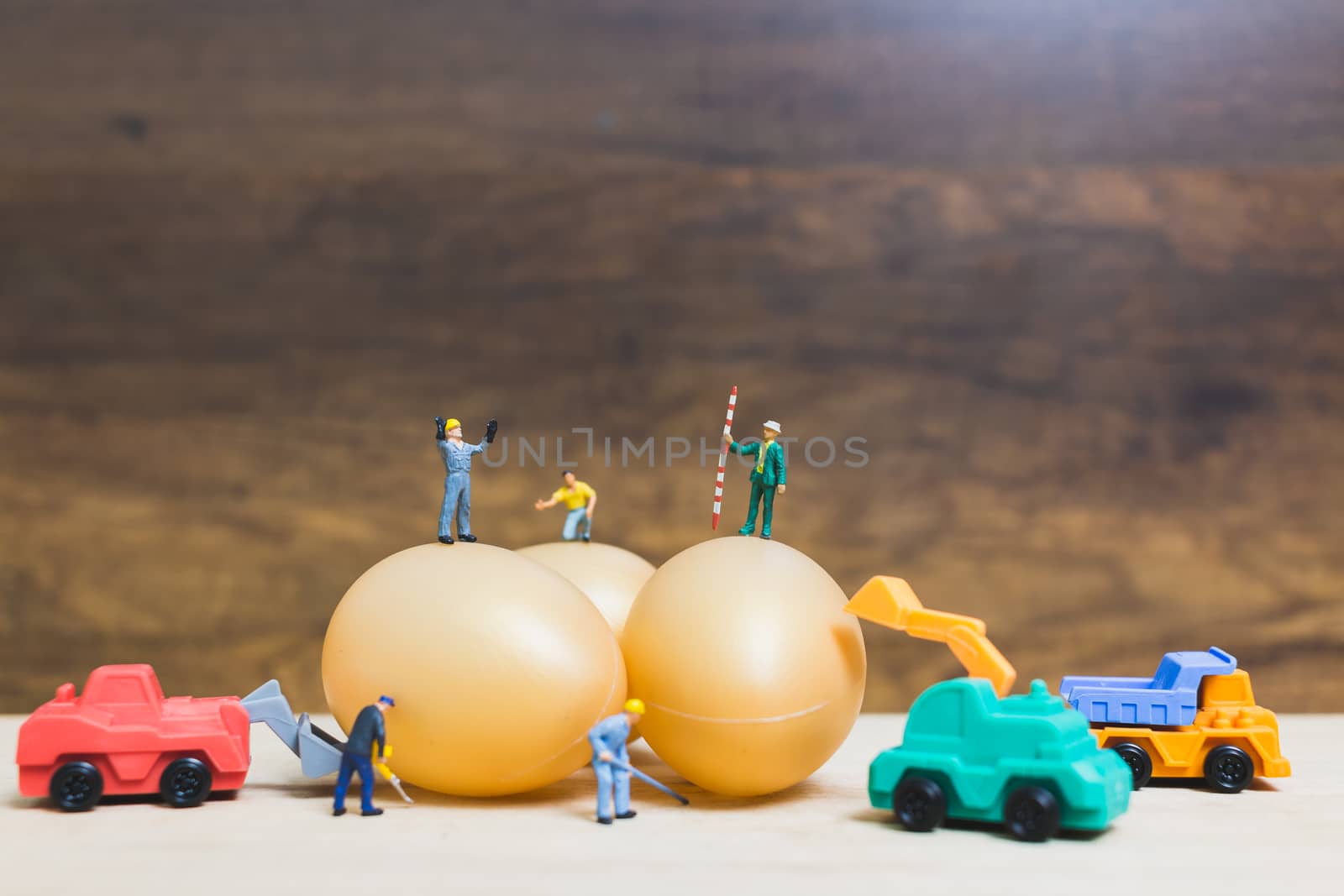 Miniature people work at Easter-eggs for Easter day on wooden background