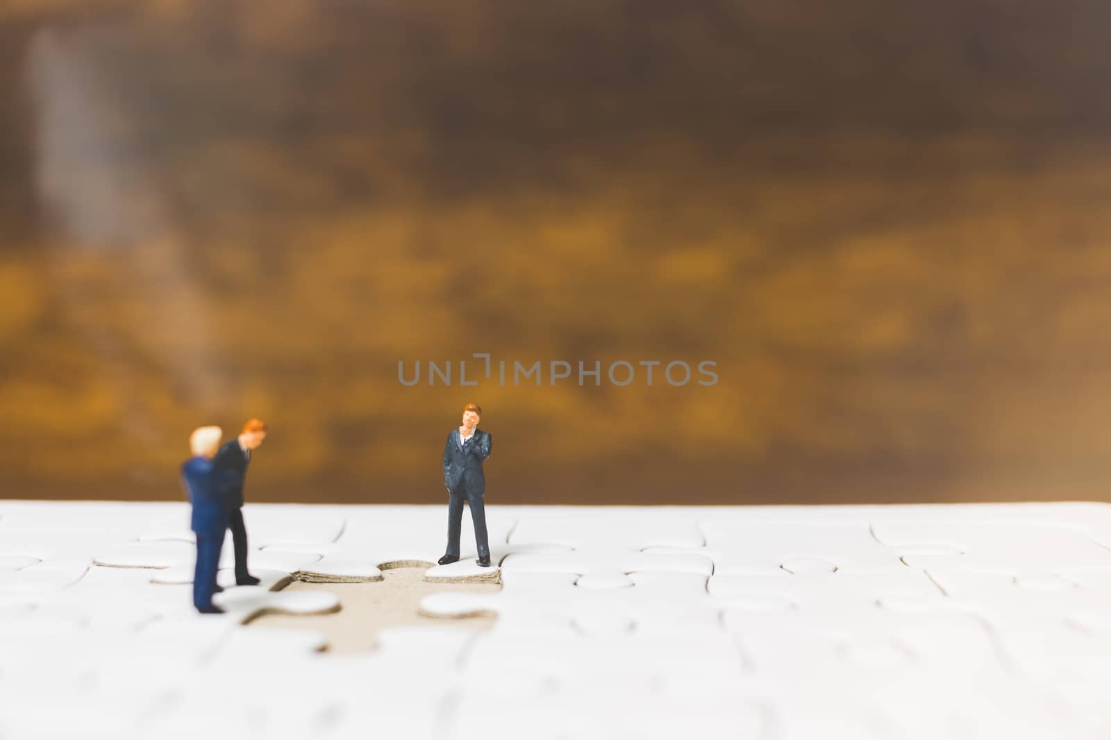 Miniature people: Businessman standing on jigsaw with wooden background : Business concept.