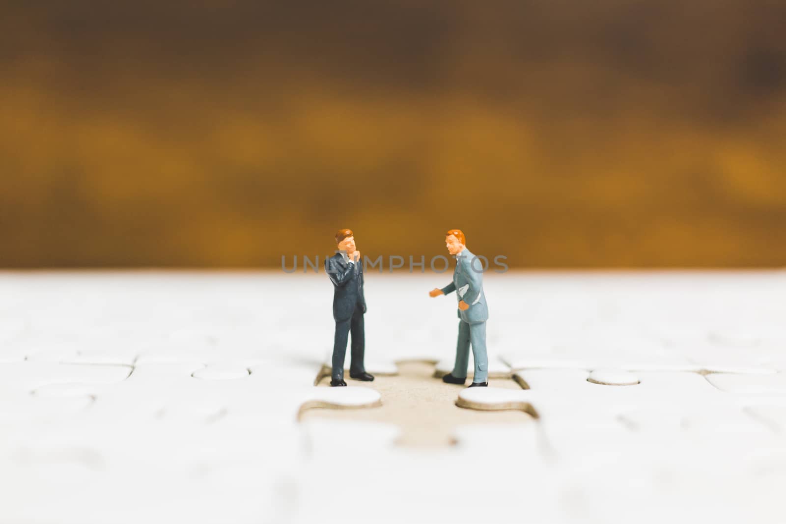 Miniature people: Businessman standing on jigsaw with wooden background : Business concept.