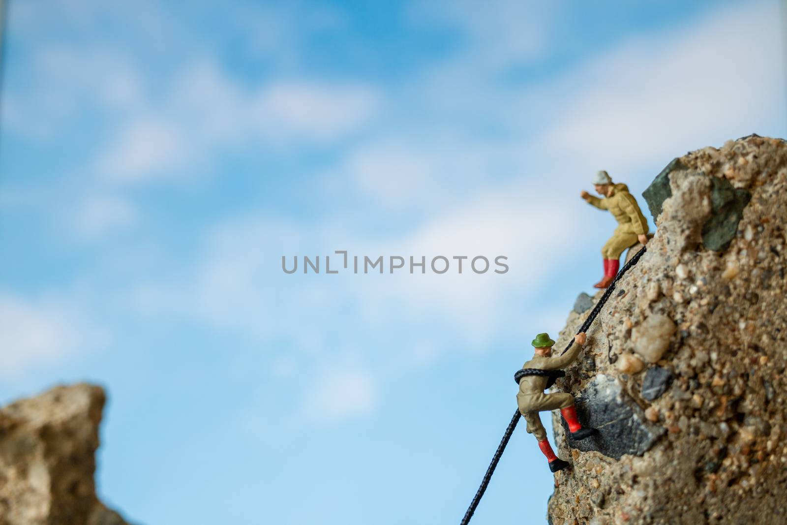 Miniature people: Hikers climbing up on the rock . Sport and leisure concept.