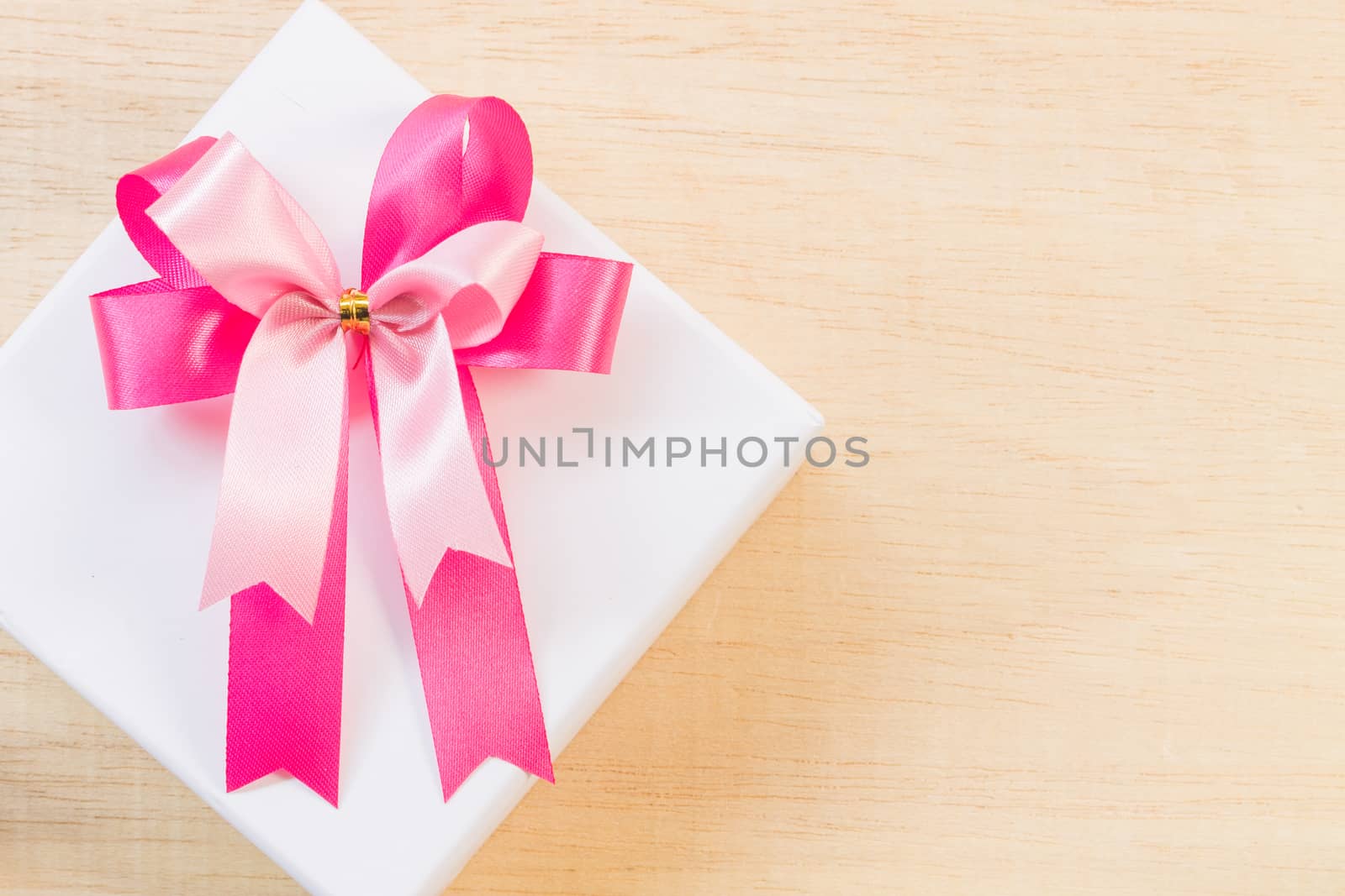 Pink ribbon bow and white gift box on wooden background