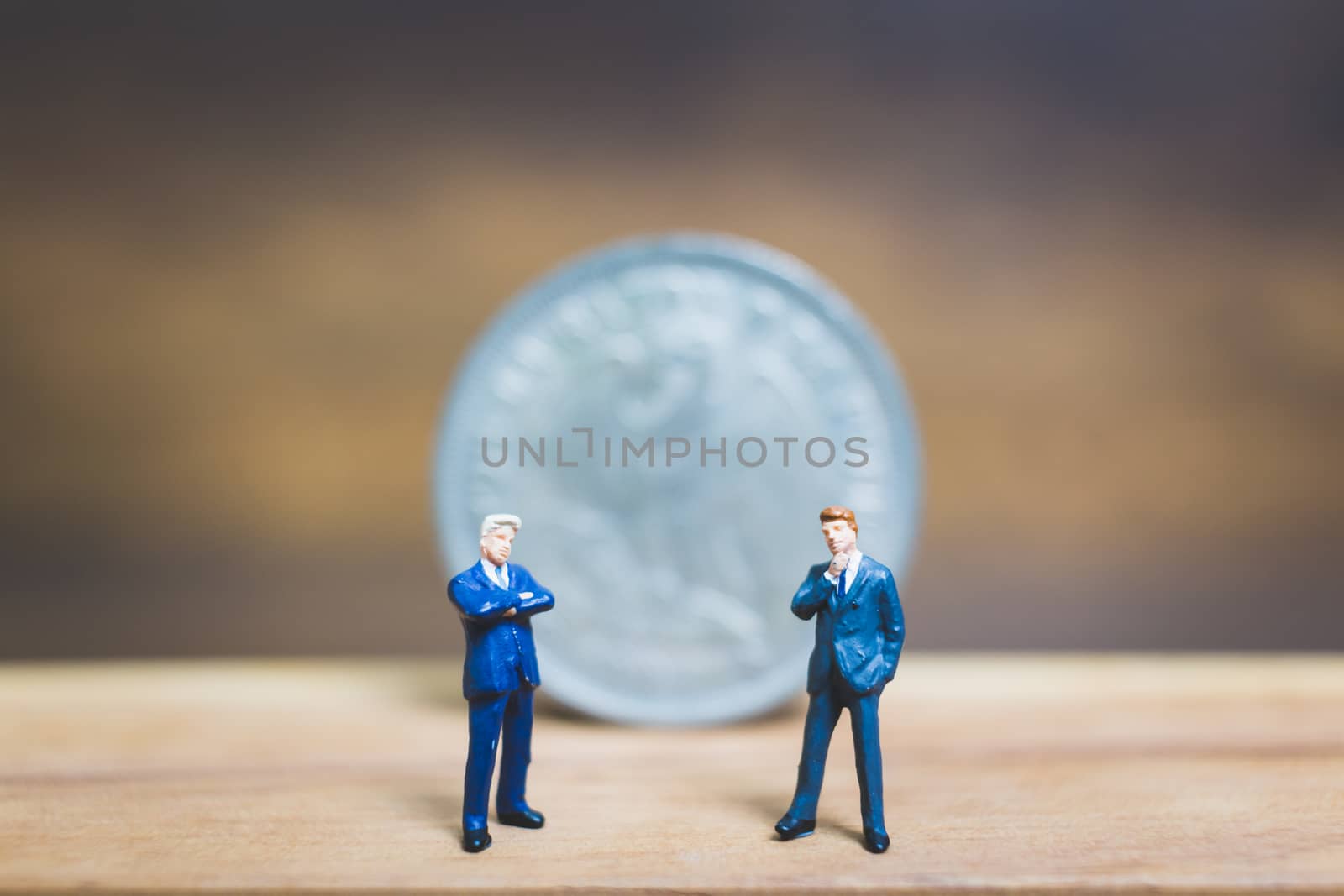 Miniature people : Businessman standing near coin with wooden background : Business concept.